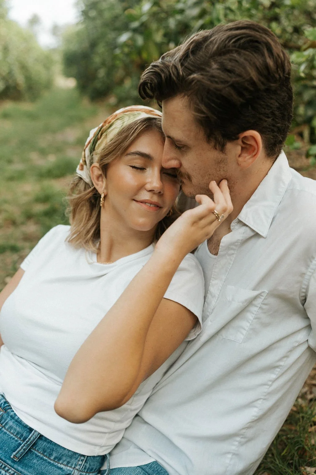 A couple sharing an intimate moment outdoors, with the woman gently touching the man's face as they lean in close to each other