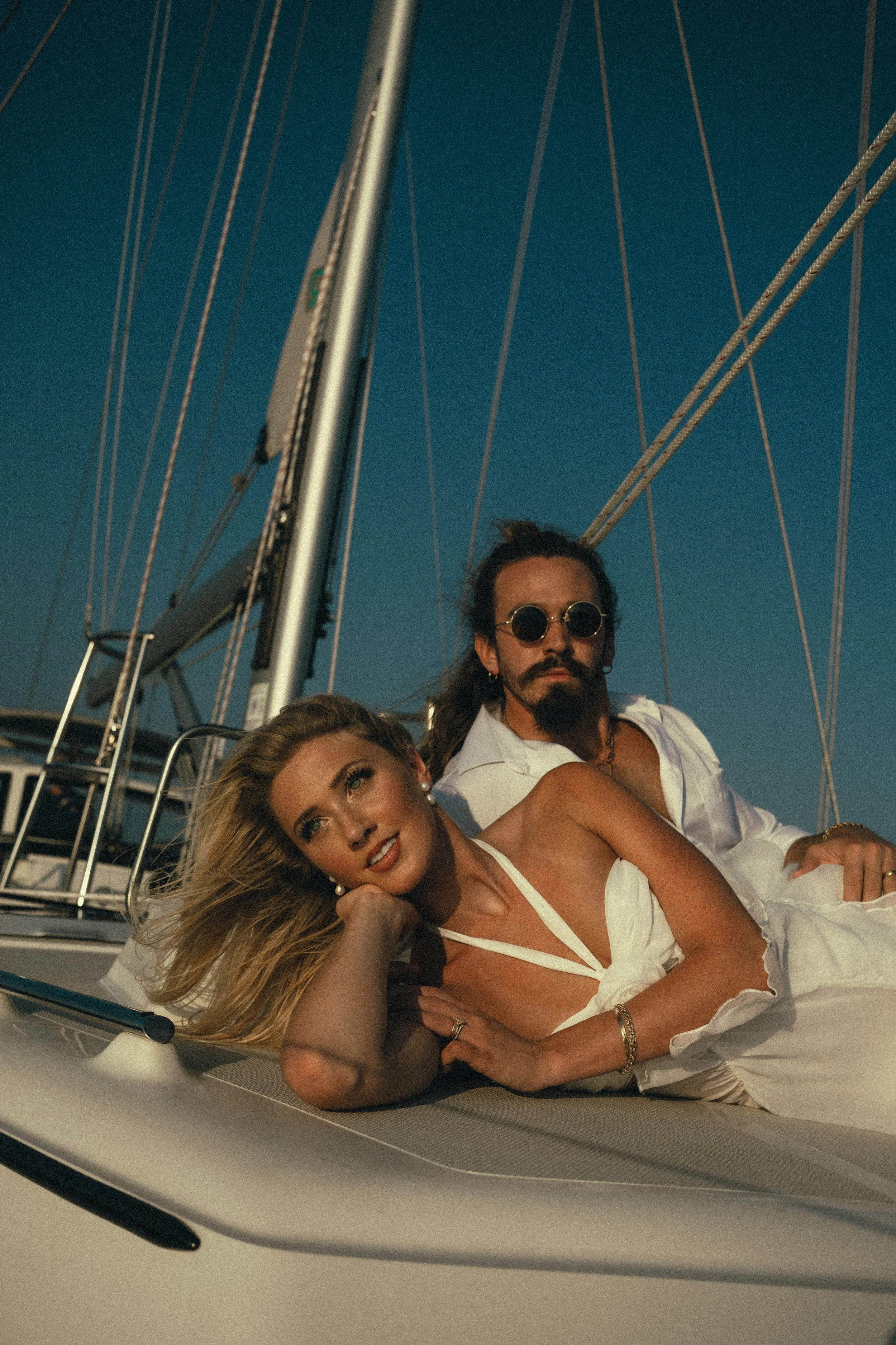 A woman and a man on a sailboat during sunset, relaxing on the deck.