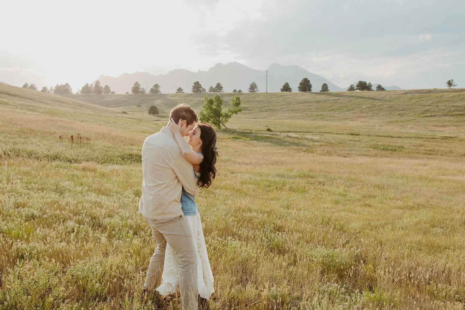 A couple embracing in a grassy field with mountains in the background during daytime.
