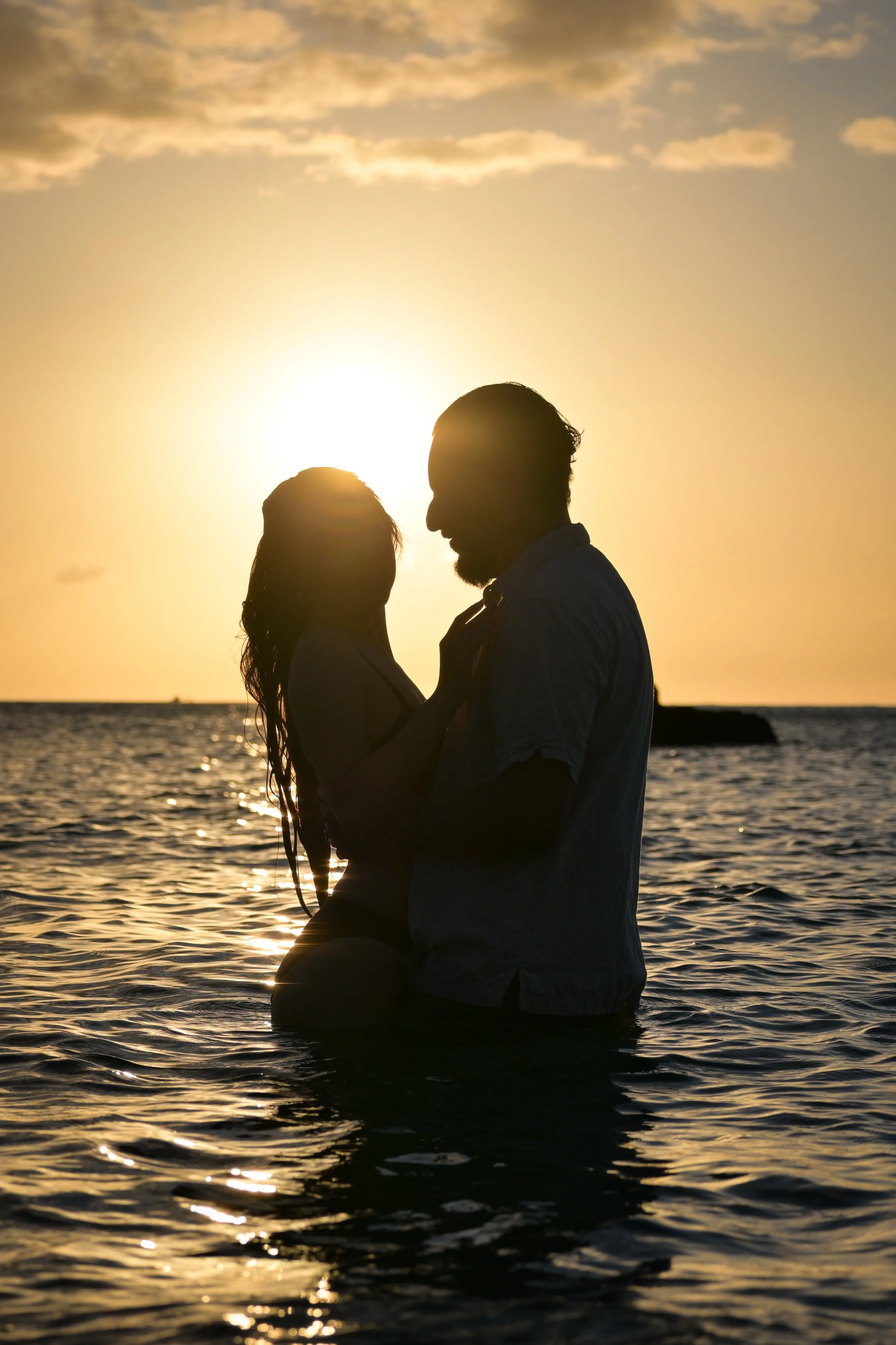 Silhouette of a couple embracing in the water at sunset with the ocean and sky in the background.