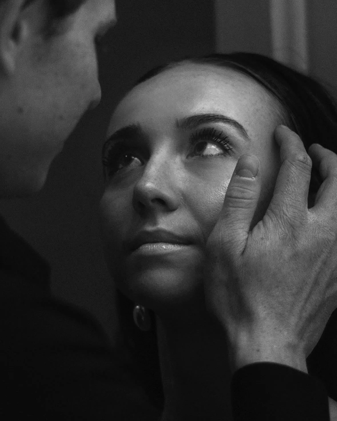 Close-up of a woman with makeup, looking up at a man touching her face gently.