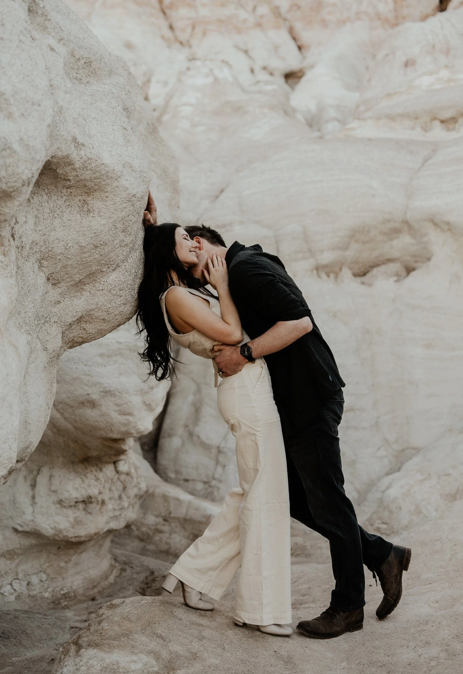 A couple in an embrace and kiss against large white rock formations.