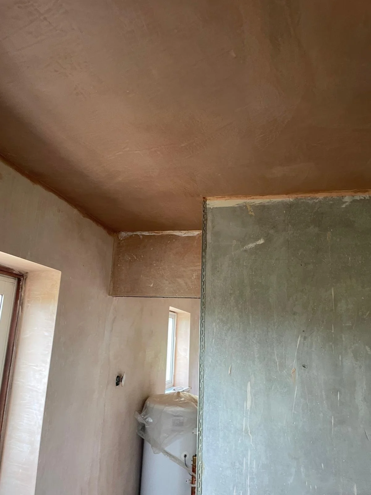 Interior of a room under construction or renovation with unpainted walls and ceiling, a window, and construction materials.