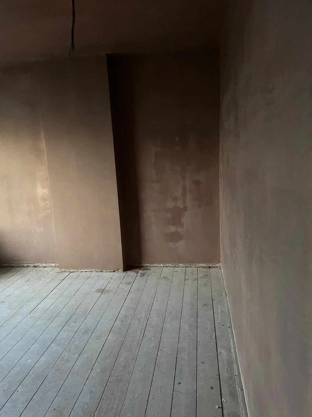 Interior of an unfinished room with plywood floors and walls that are partially painted or plastered.