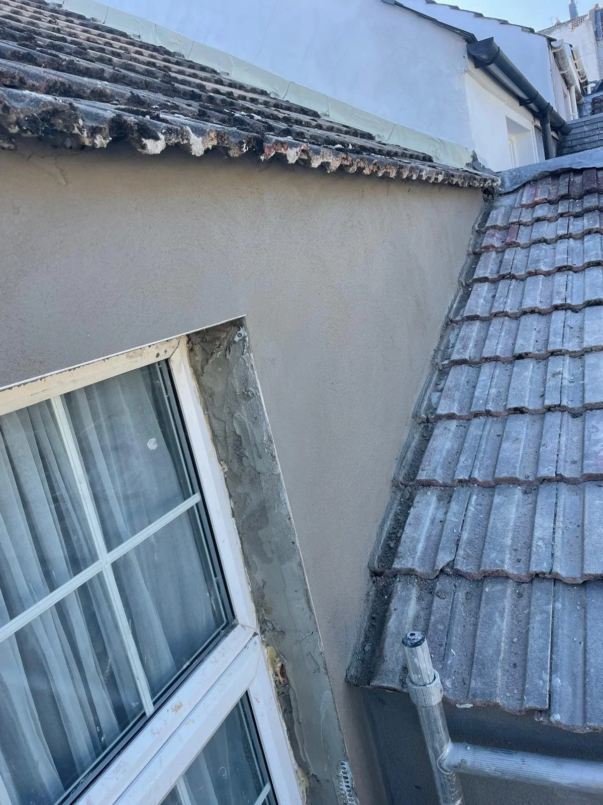 Side of a building with a window, a newly repaired or plastered wall section, and a tiled sloped roof.