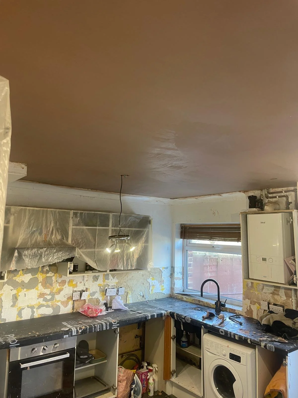 Kitchen under renovation with unfinished walls, partially installed countertop, cleaning supplies, and a washing machine.