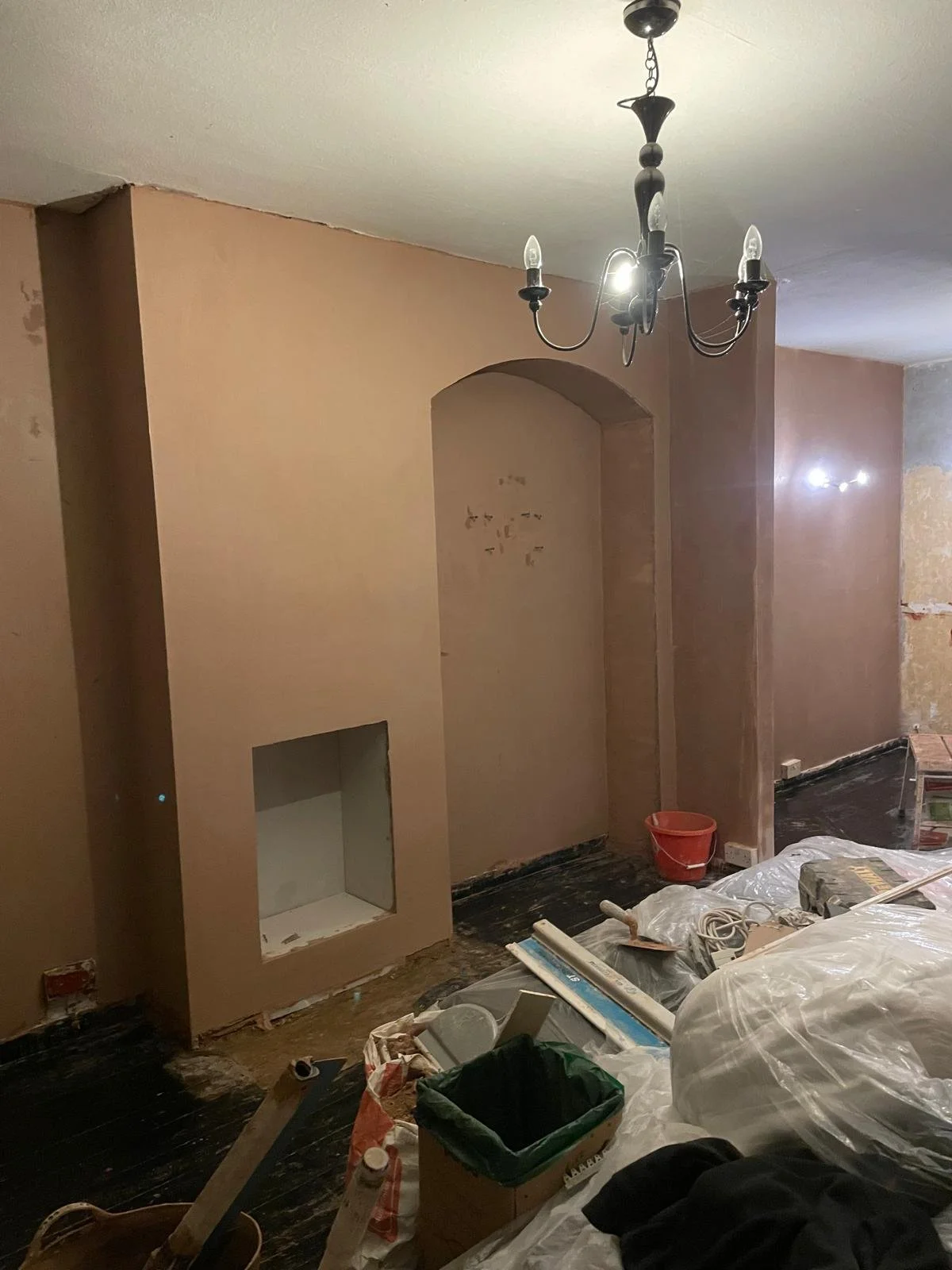 Interior room under renovation with a chandelier, pink walls, and construction tools and materials on the black floor.