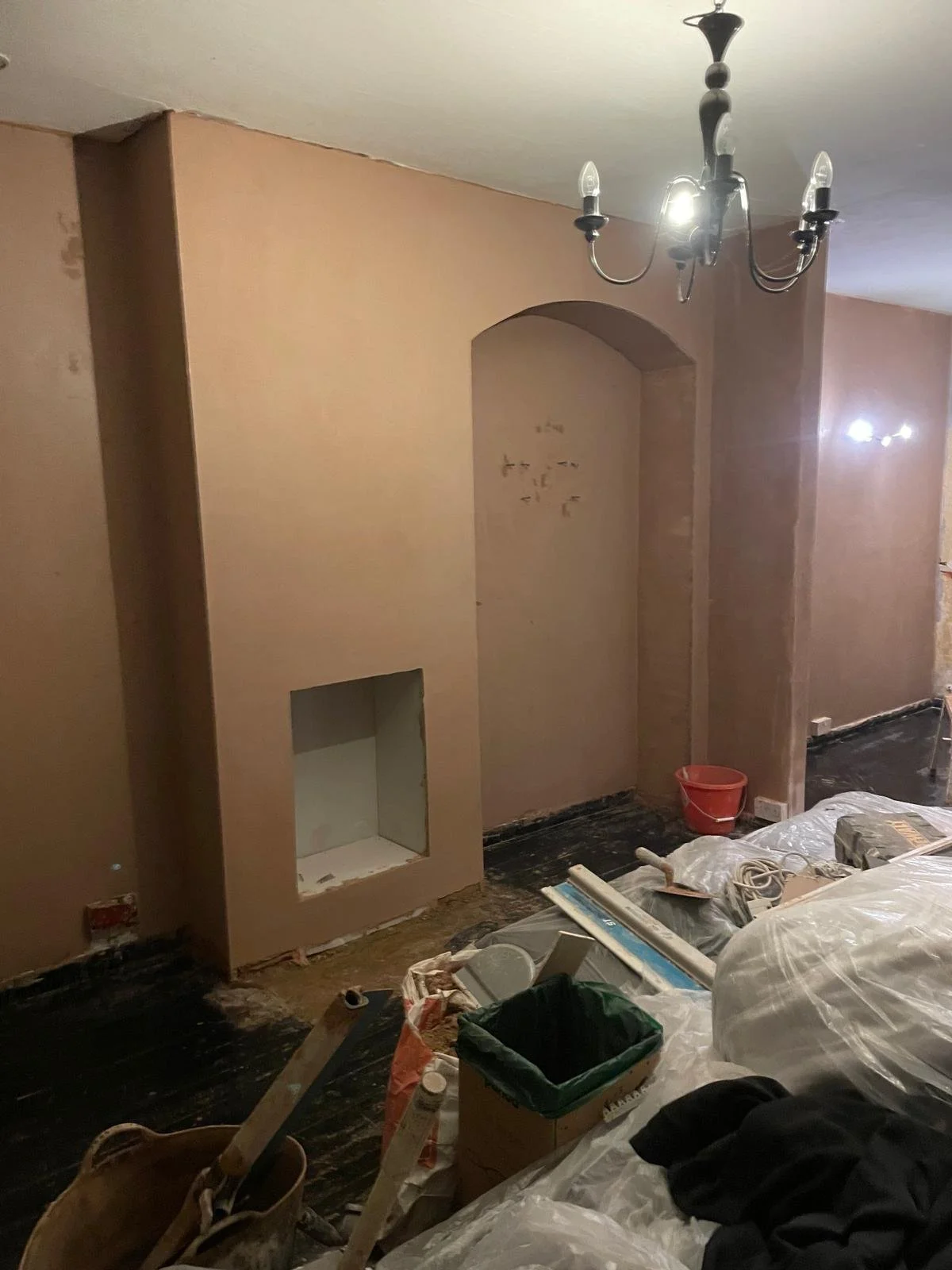 Living room under renovation with partially painted walls, unfinished features, and construction tools and supplies on the floor.