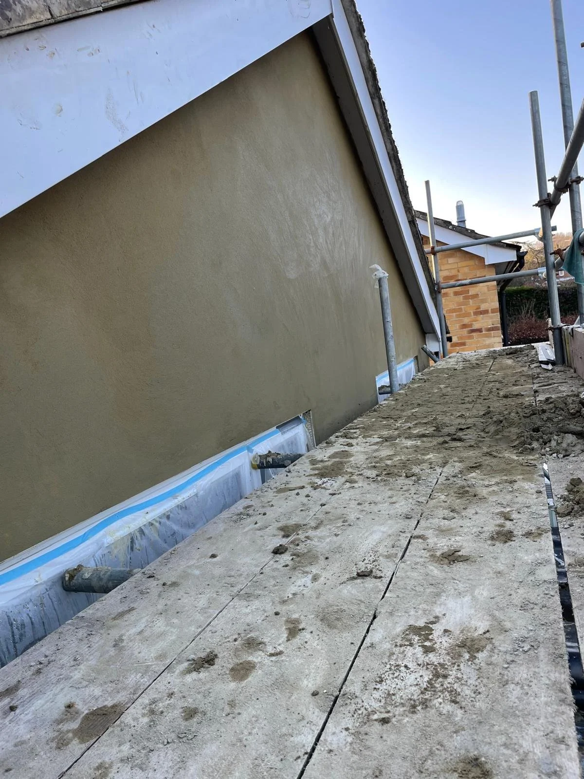 Exterior construction site with beige wall, scaffolding, and a weathered wooden walkway.