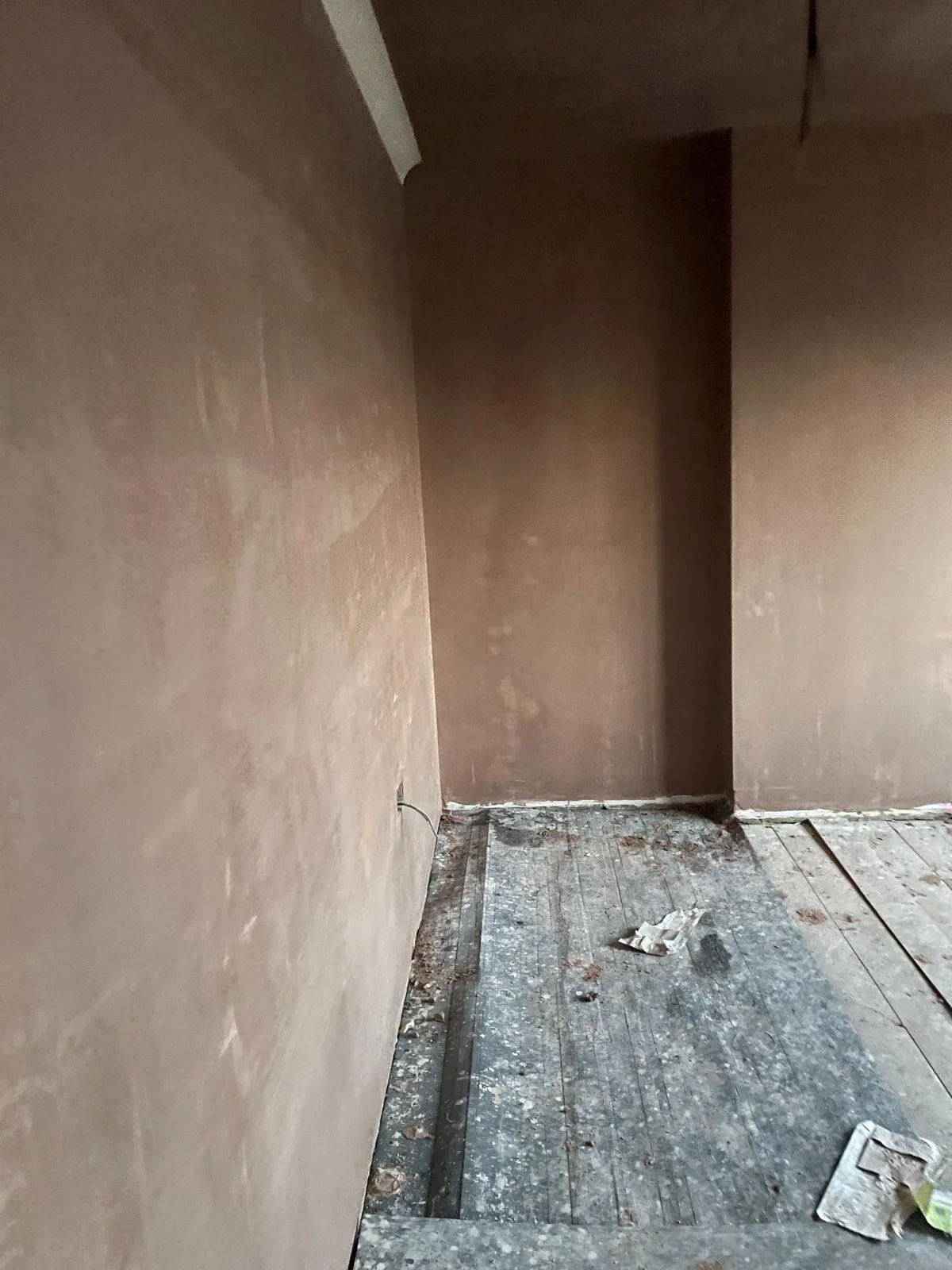 Interior of a room under construction with unfinished walls and worn, dusty floor with debris.