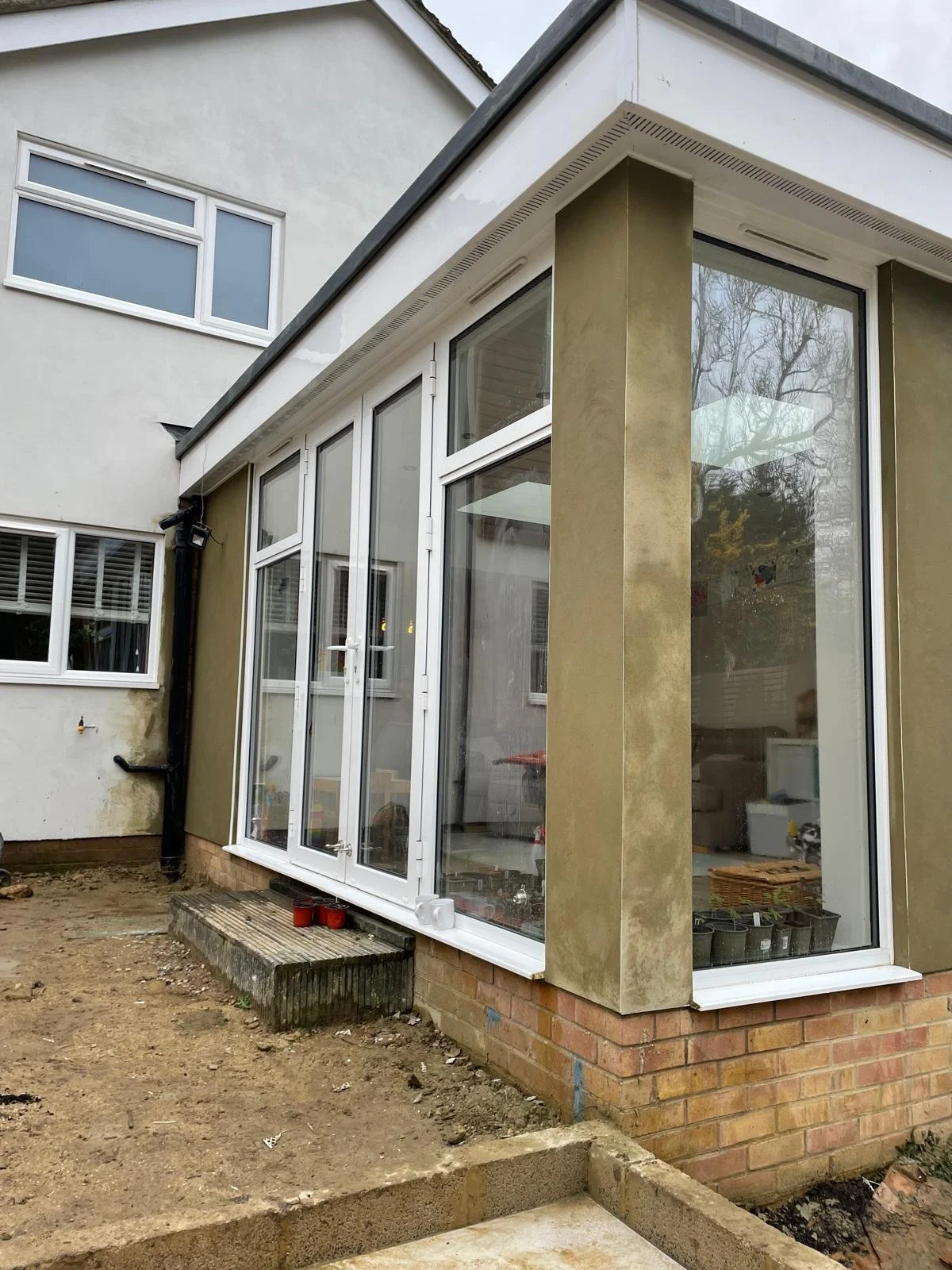 Under construction back porch of a house with large glass windows and door, brick foundation, and a small wooden step.