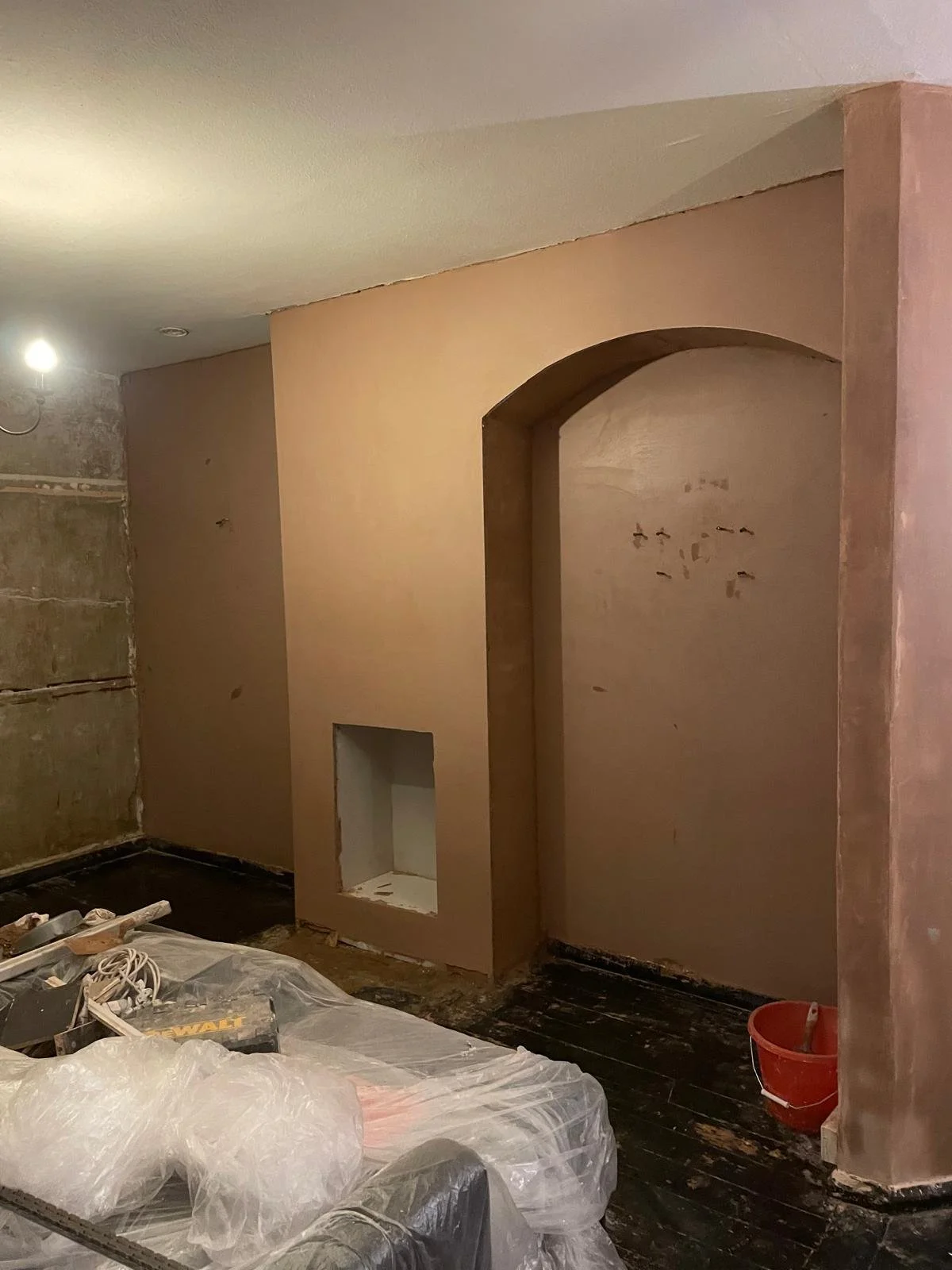 Interior room under renovation with partially finished wall, open archway, and construction tools on the floor.