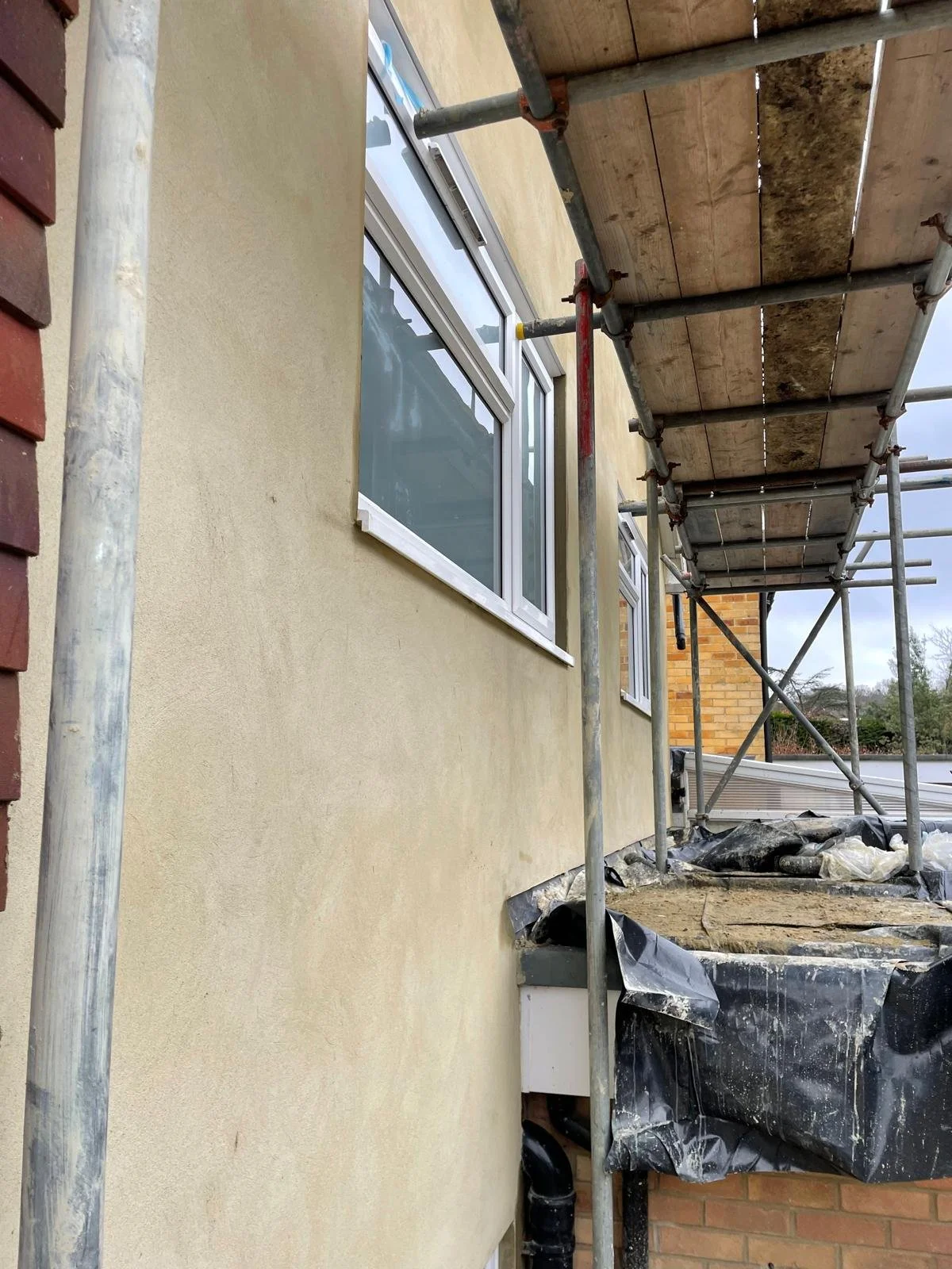Exterior wall of a building under construction with removed window, scaffolding, and construction materials nearby.