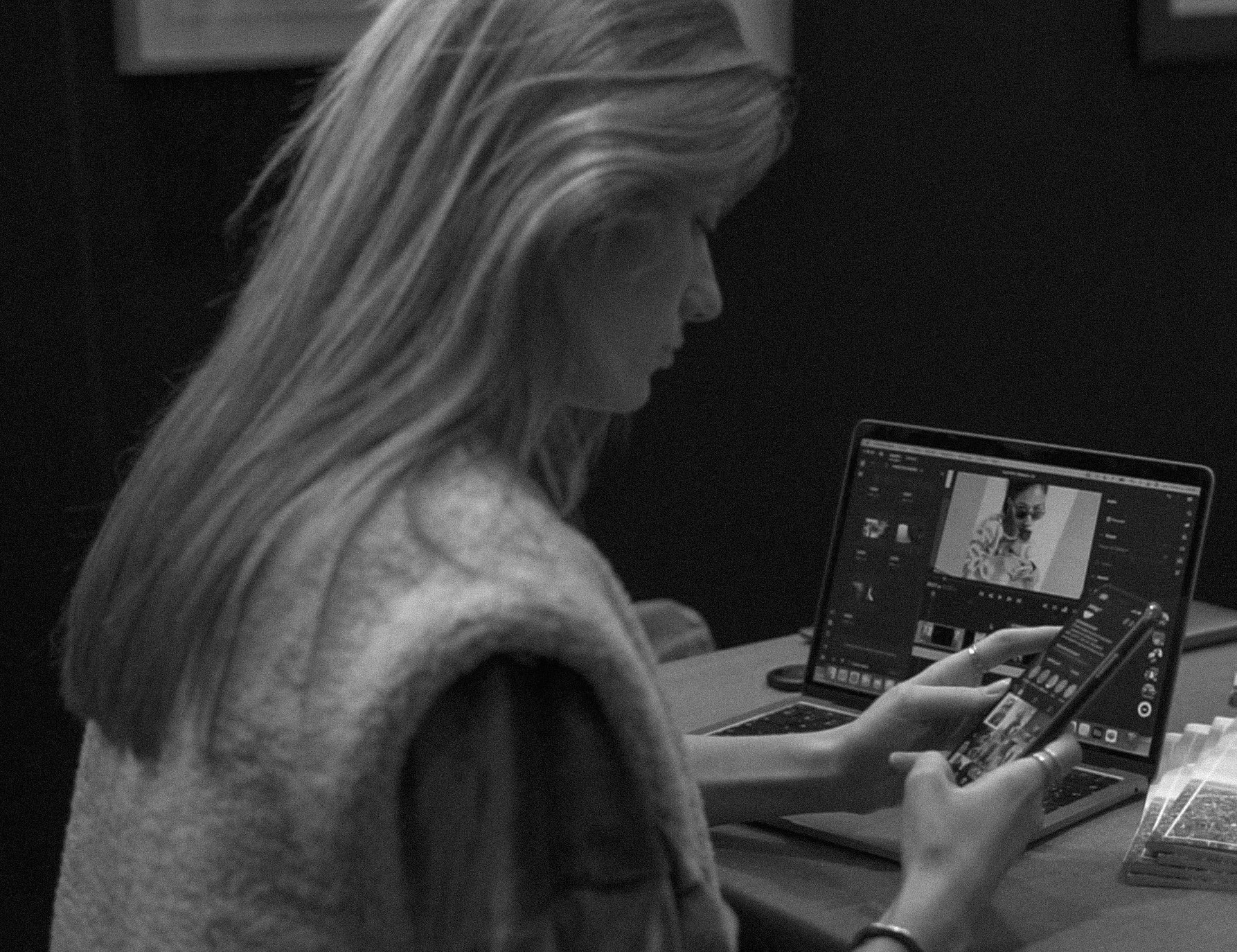 Une femme à long cheveux chute, regarde un téléphone et utilise un ordinateur portable avec un logiciel de retouche photo.