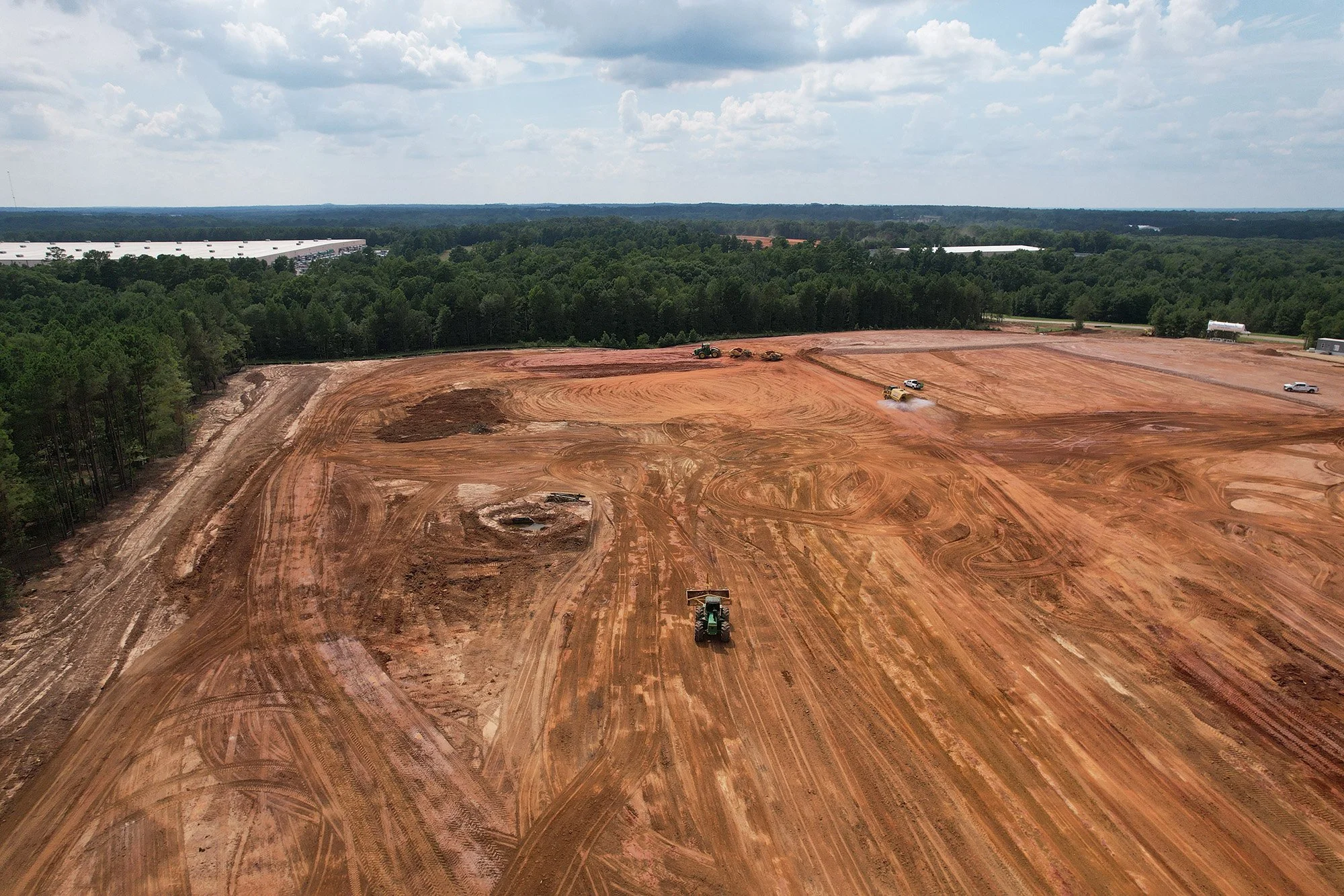 A vast dirt field occupied by a tractor and a bulldozer, suggesting ongoing earth-moving operations.