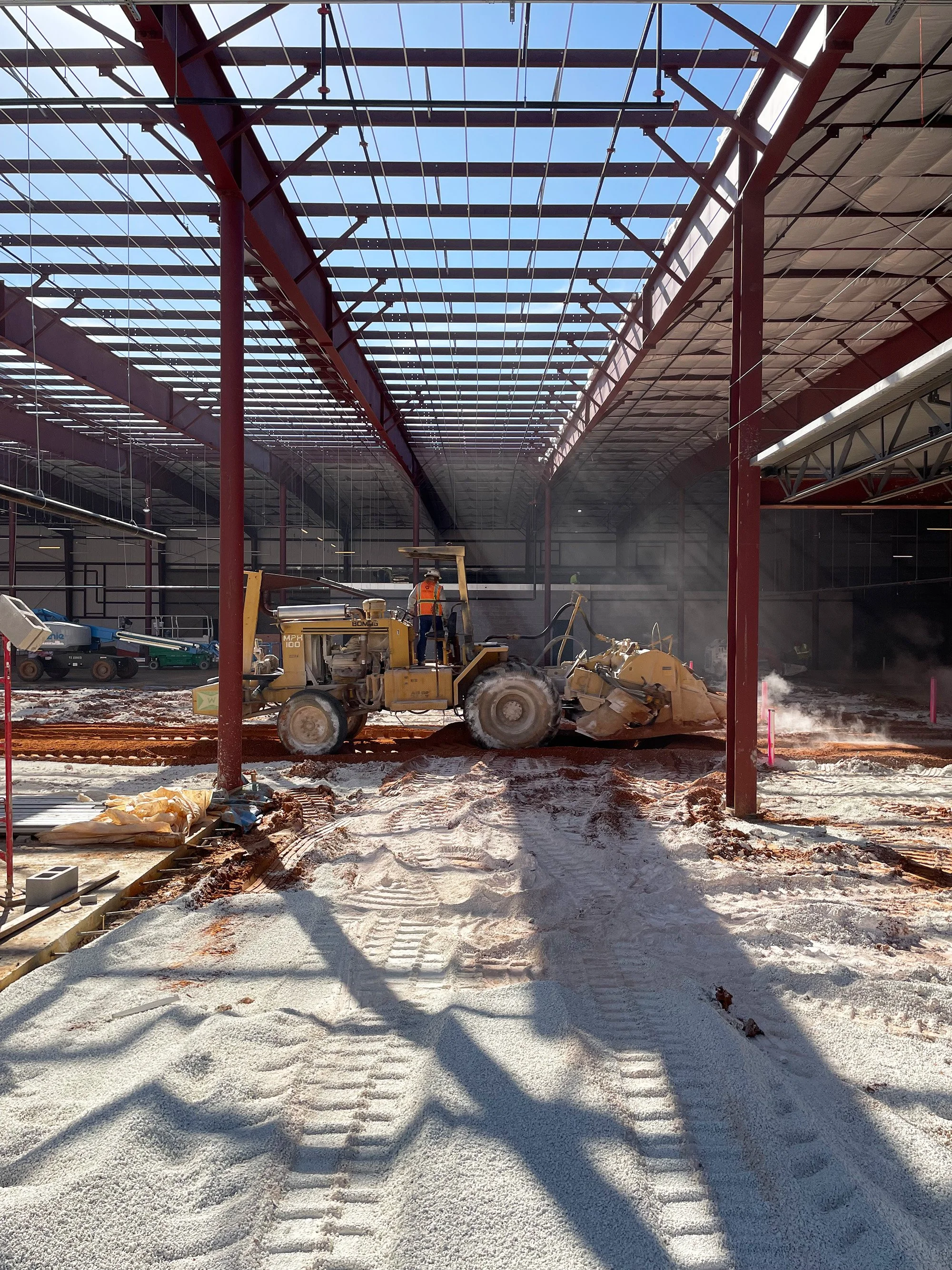 Inside an industrial building, construction workers are seen working alongside a bulldozer, contributing to the construction project.