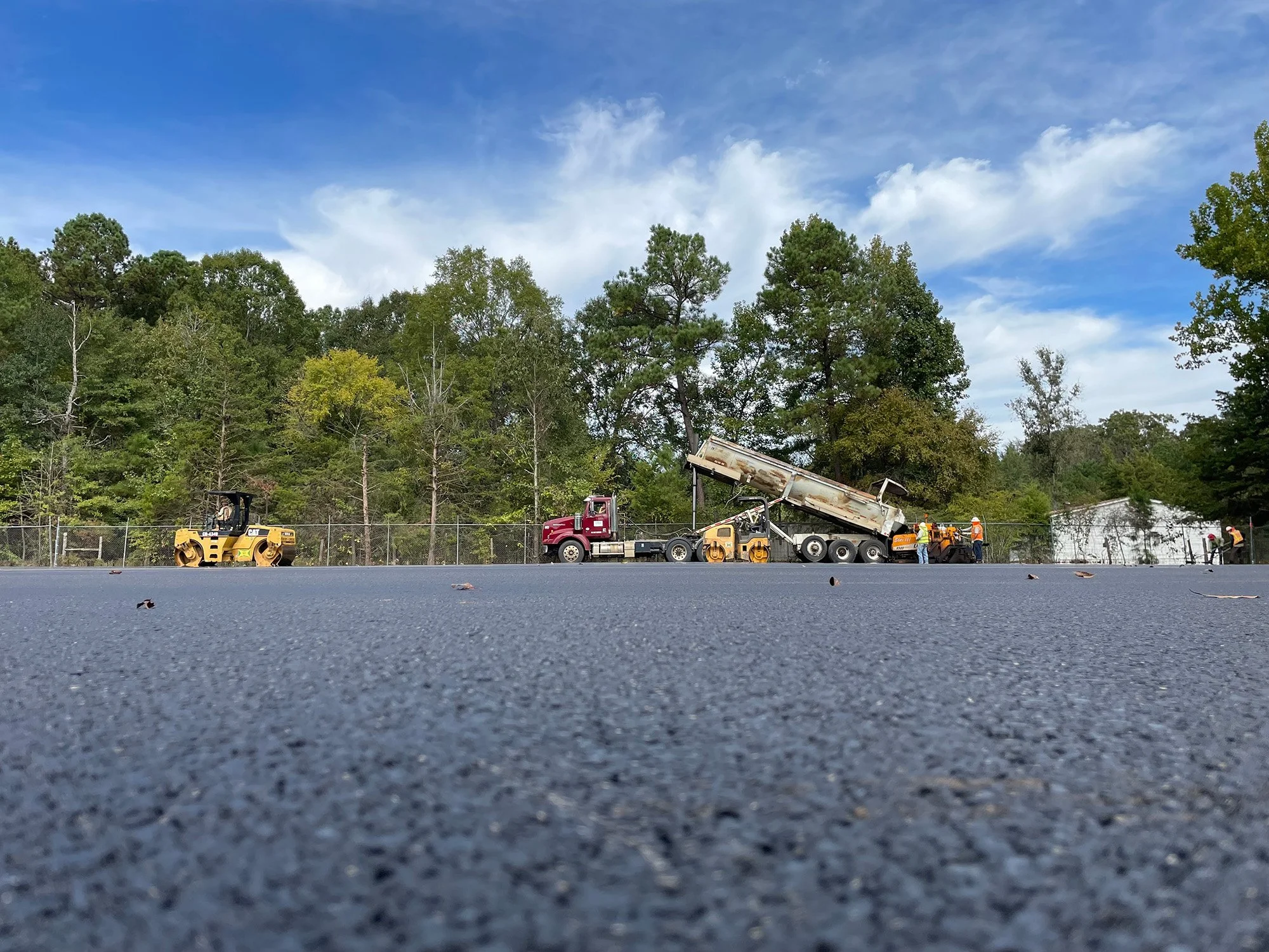 A construction crew is laying asphalt on a new road, with workers and machinery actively engaged in the process.