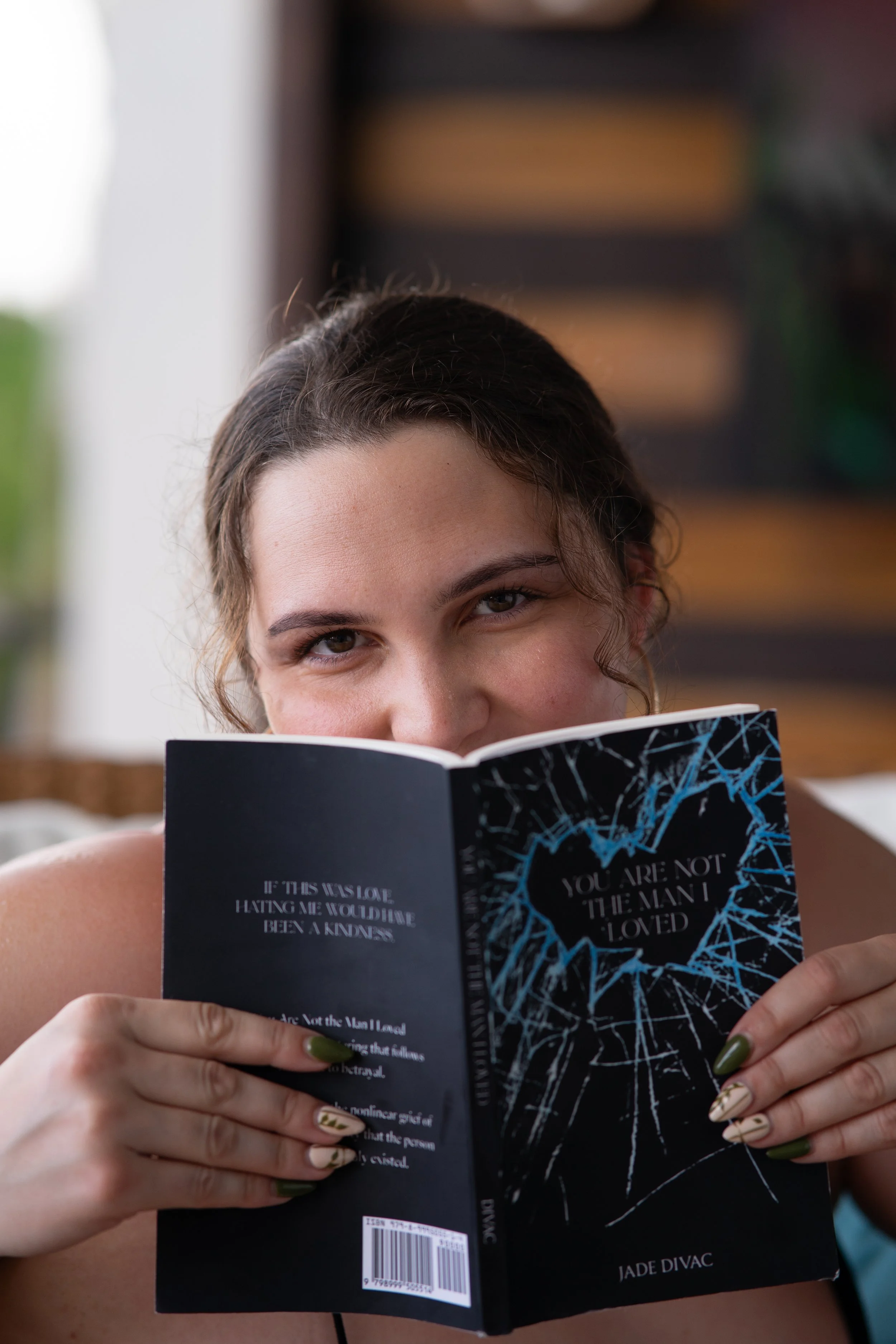 Jade’s upper face is exposed, the lower half behind an opened copy of her book You Are Not The Man I Loved
