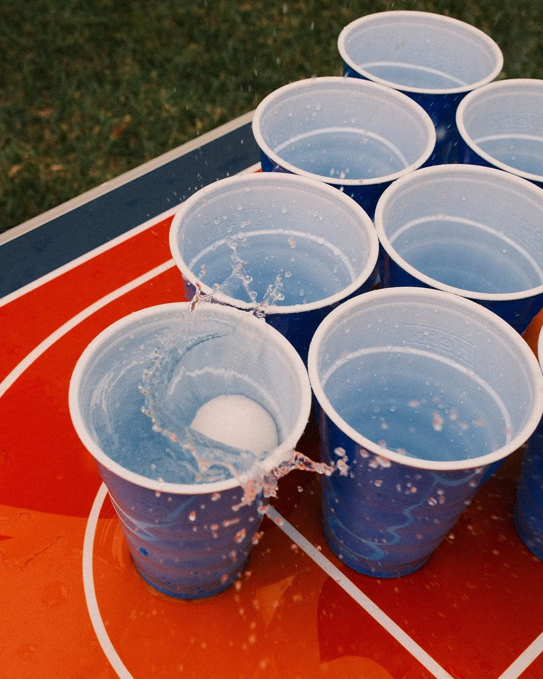 Multiple red cups arranged in a formation on a table, with a stylized background featuring a white circle and blue and red shapes.