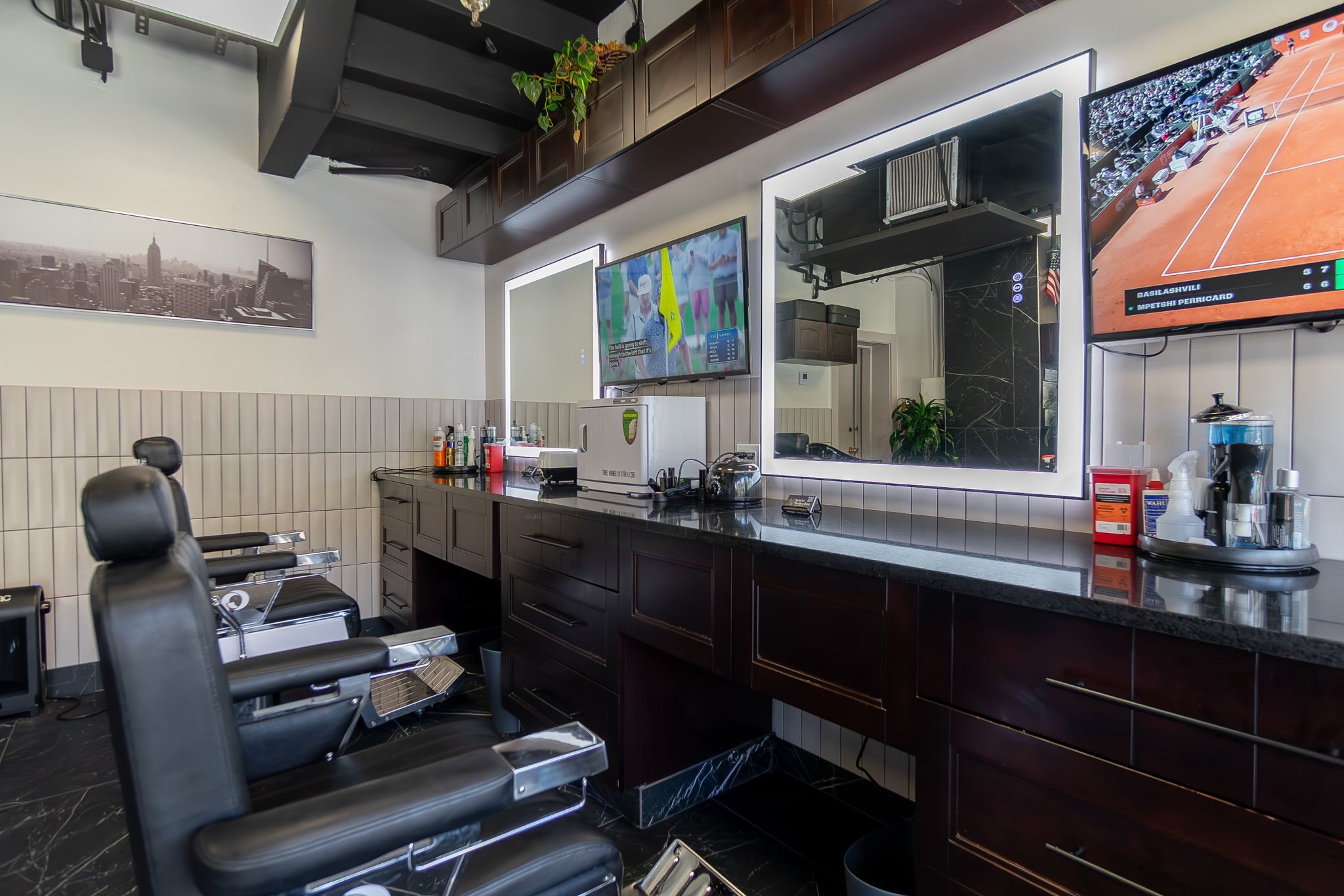 Barber shop with black chairs, dark wood cabinetry, and televisions showing sporting events.