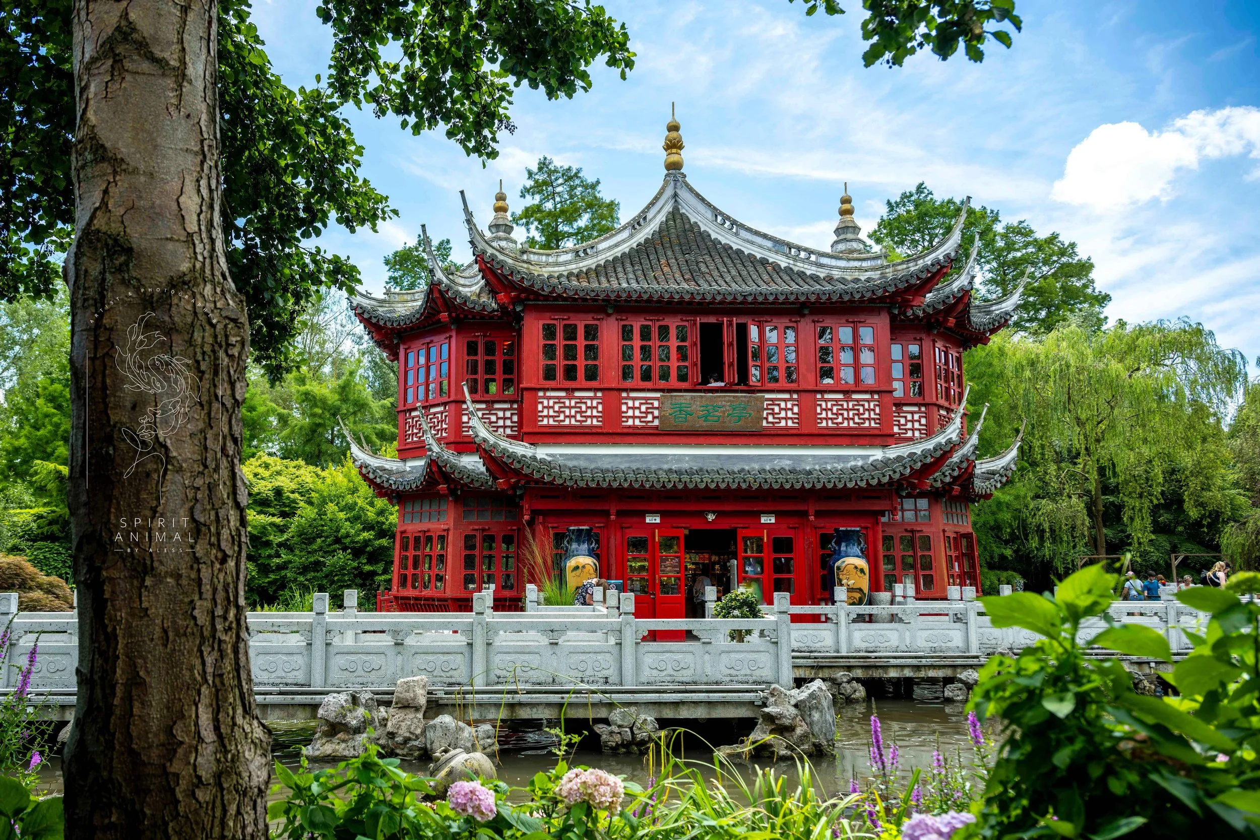 Traditionelles chinesisches Gebäude in einem Park mit Wasser und Pflanzen, rotes zweistöckiges Holzgebäude mit chinesischen Zeichen, vor einem blauen Himmel mit einigen Wolken, Fotografie von SPIRIT ANIMAL