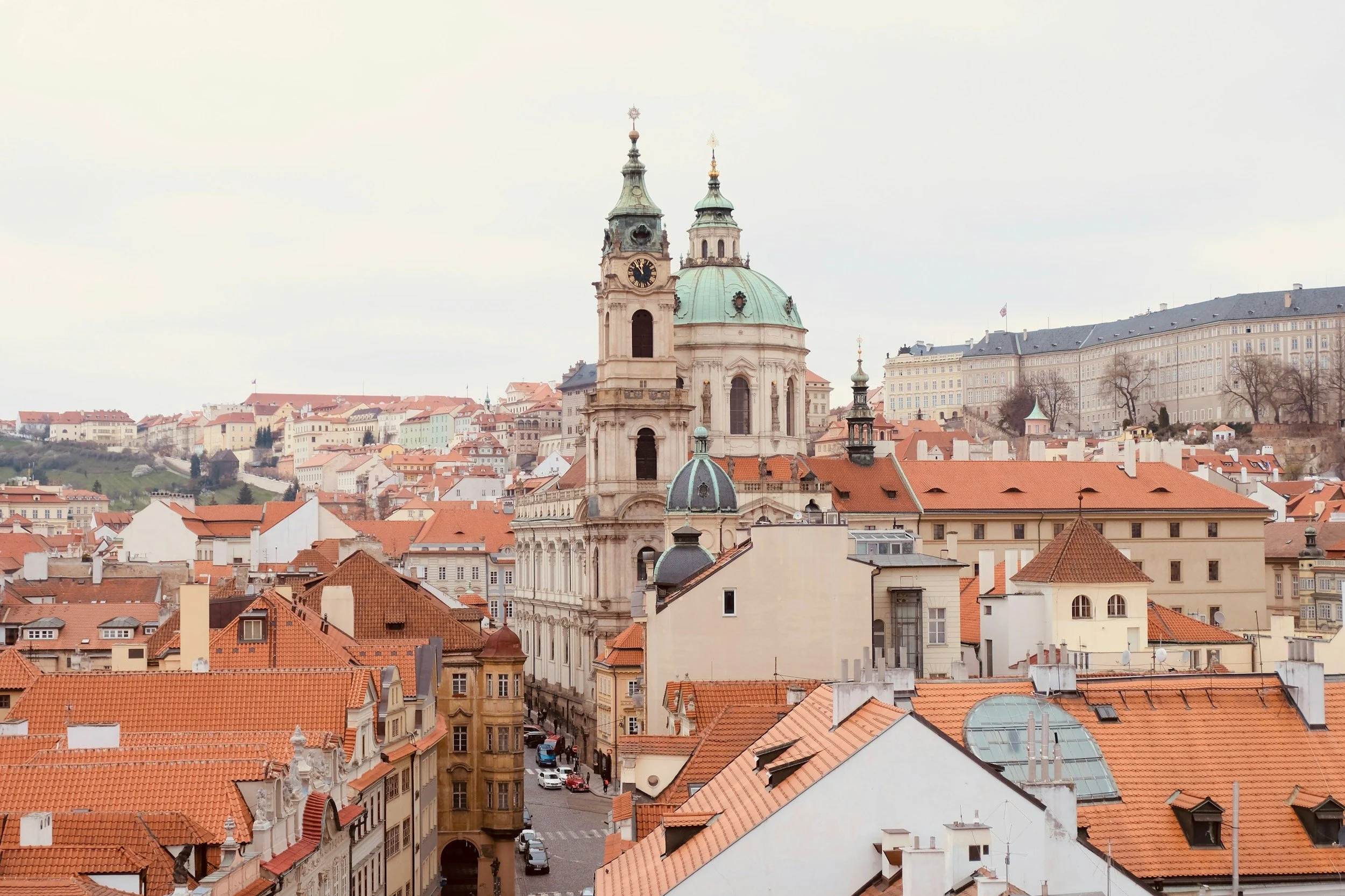 Aerial view of Prague's historic skyline with St. Nicholas Church, featuring red rooftops and Baroque architecture.