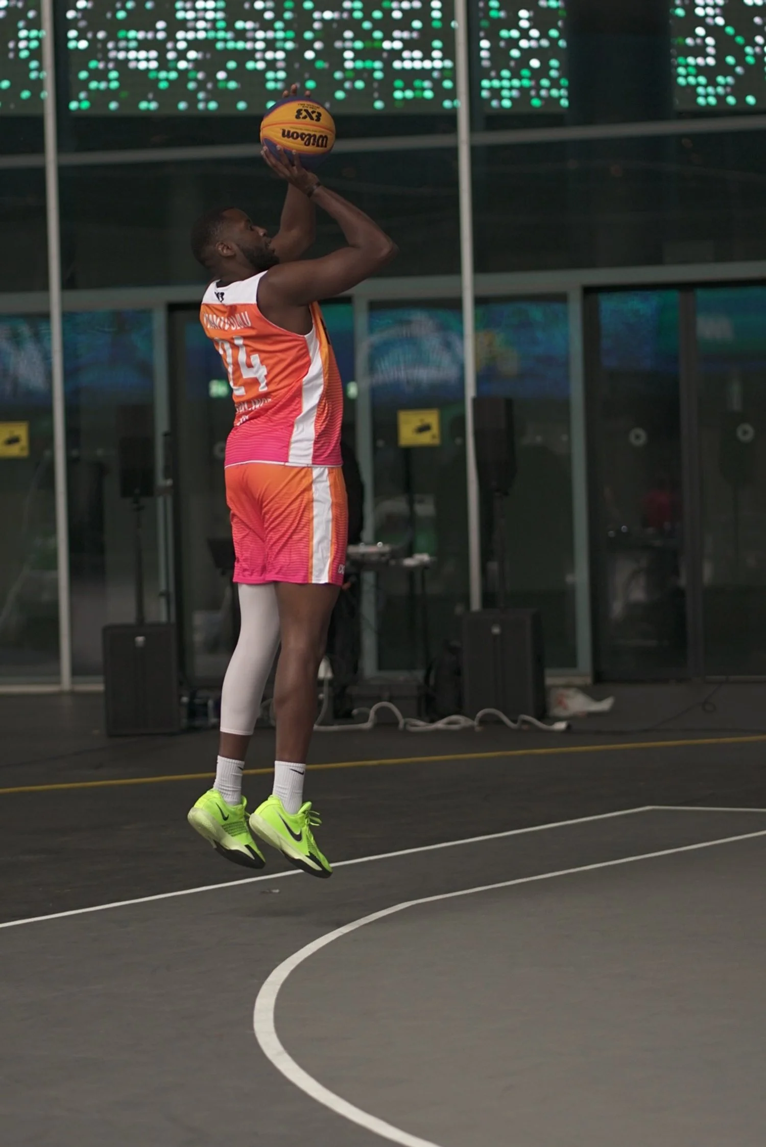 Basketballspieler springt auf einen Basketballkorb und bereitet einen Wurf vor, im Hintergrund eine digitale Anzeigetafel.