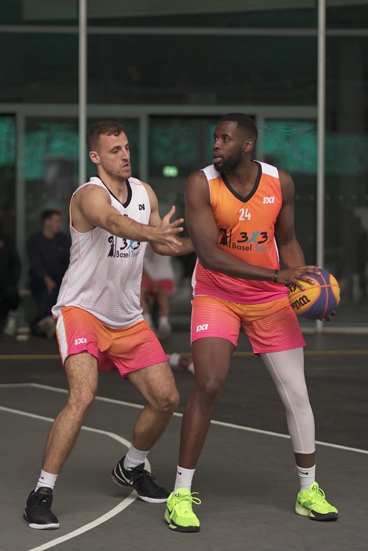 Zwei Basketballspieler im Wettkampf während eines Spiels auf einer Indoor-Court, einer mit Ball, beide in bunten Trikots und Shorts.
