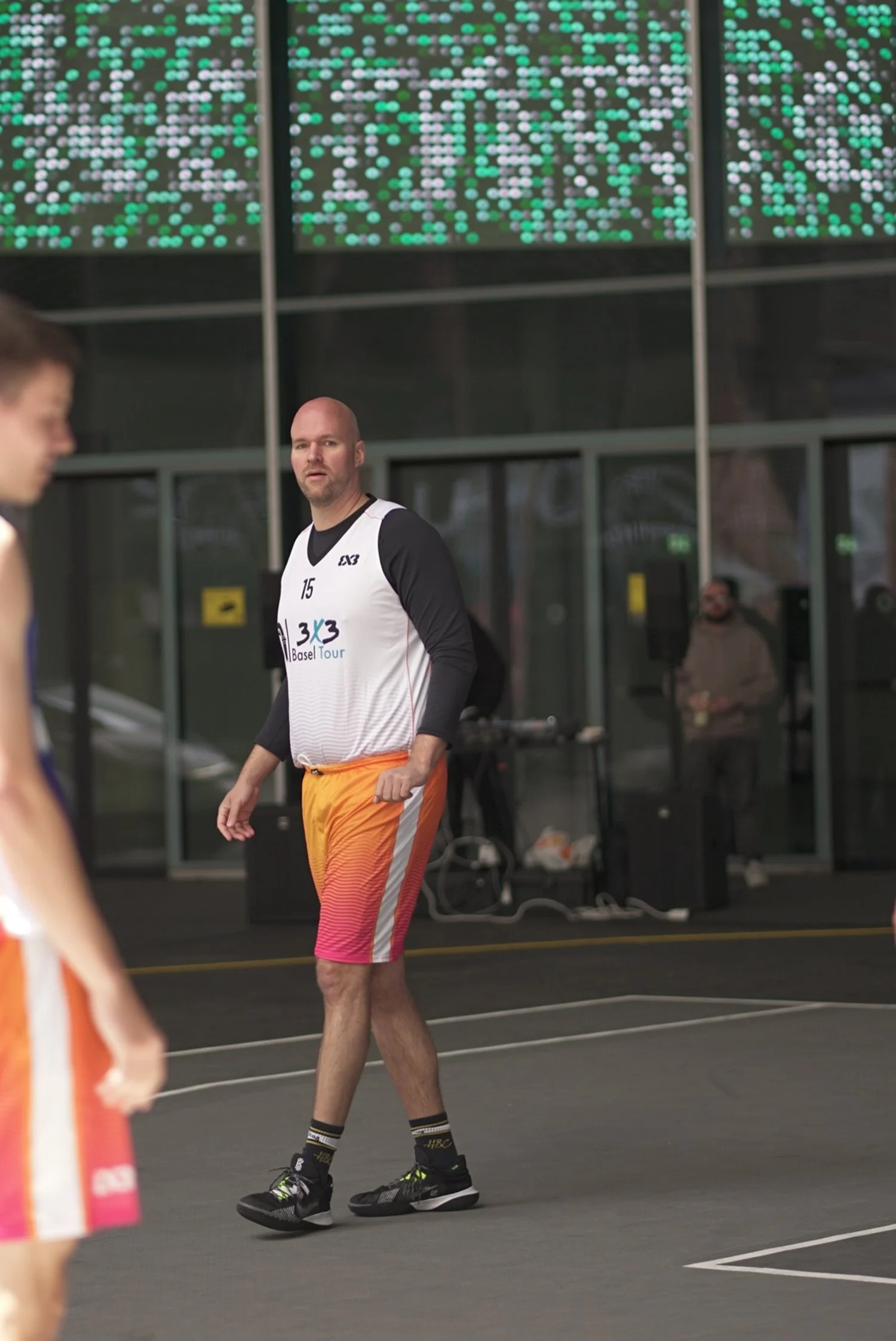 Basketballspieler in einem Turnier, im Hintergrund eine Anzeigetafel mit grünen Punkten, im Innenraum eines Basketballstadions.