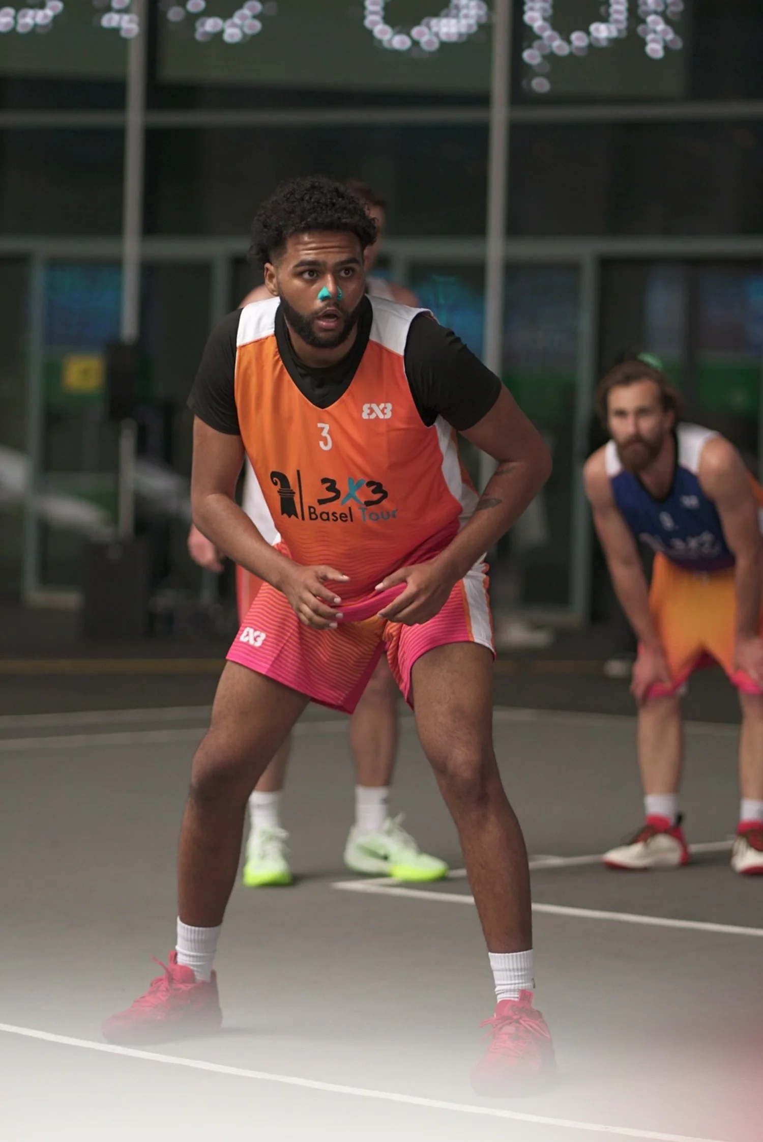 Basketballspieler in Vorbereitung, trägt orange-rote Trikot mit der Nummer 3, steht auf einem Hallen-Basketballfeld.