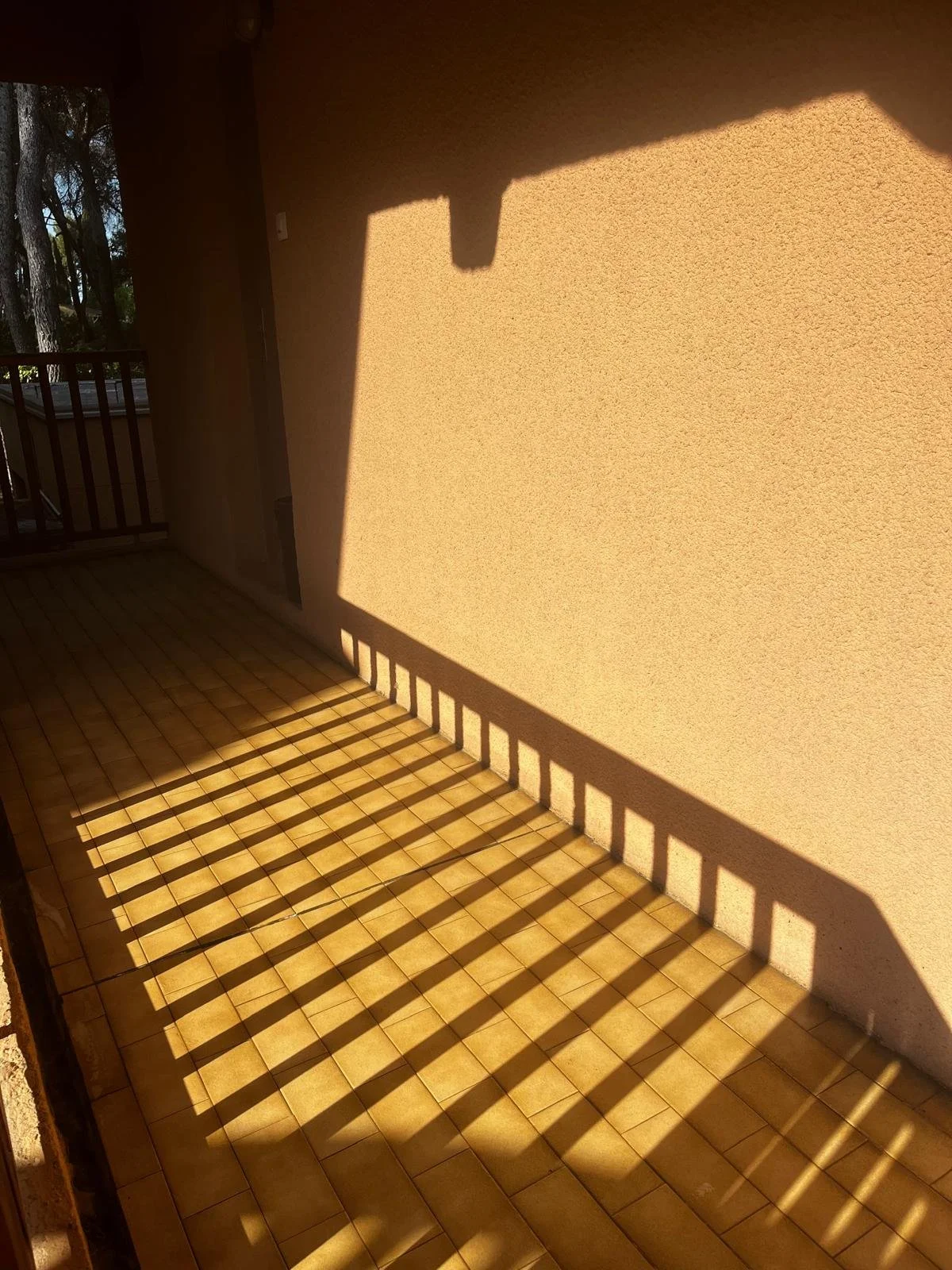 Ombre d'une balustrade sur un mur beige avec un sol carrelé, création de lignes de lumière et d'ombres.