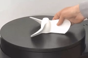 Person placing a white 3D-printed figure on a round black platform.