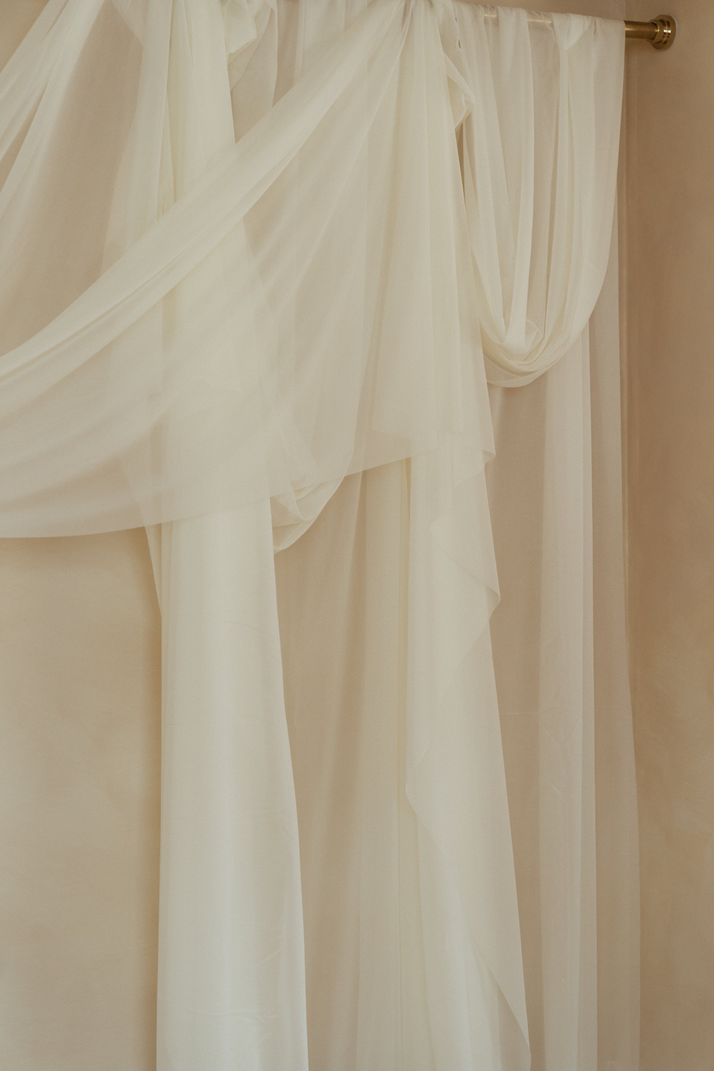 Close-up of white wedding or dress curtains with draped sheer fabric, hanging from a gold curtain rod in a rentable creative photo studio in East Grand Rapids Michigan.
