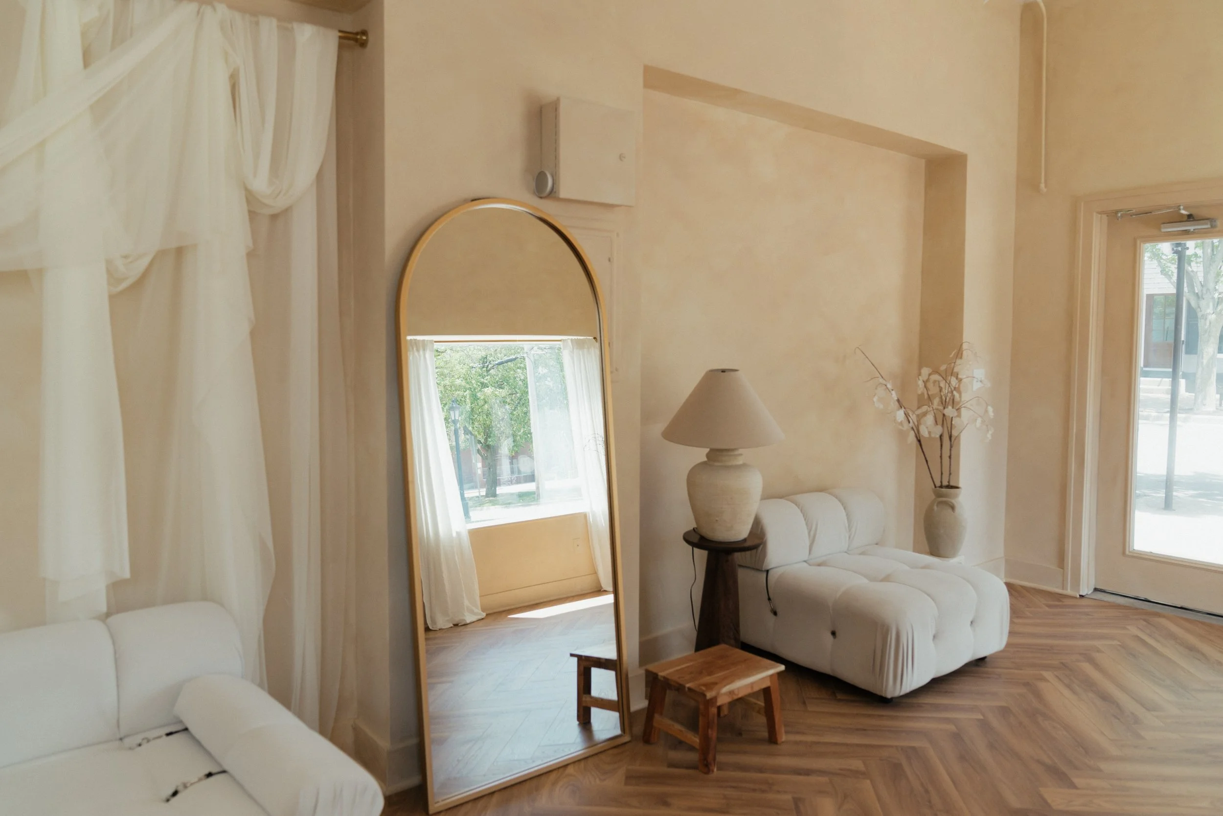 gold mirror herringbone floors plush white couch white drapery wooden stool neutral lamp Grand Rapids photo studio
