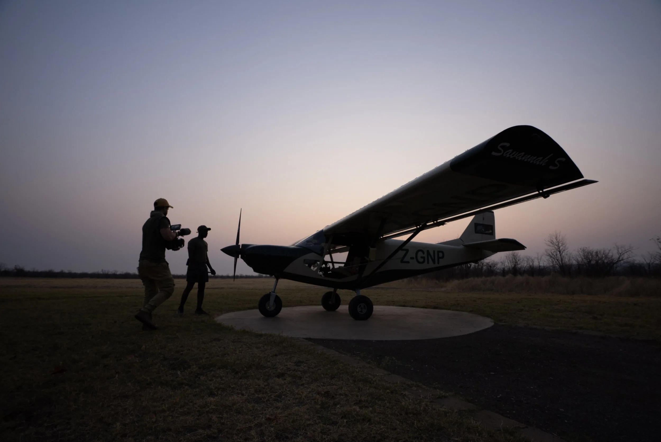 Matt Blair, conservation filmmaker, at sunrise filming a conservation pilot near a small plane on a tarmac in Gonarezhou National Park, Zimbabwe.