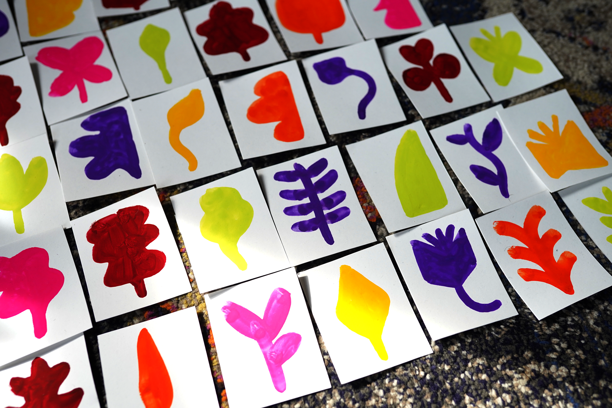 Assorted colorful paper cards with painted leaf and heart shapes spread out on a textured surface.