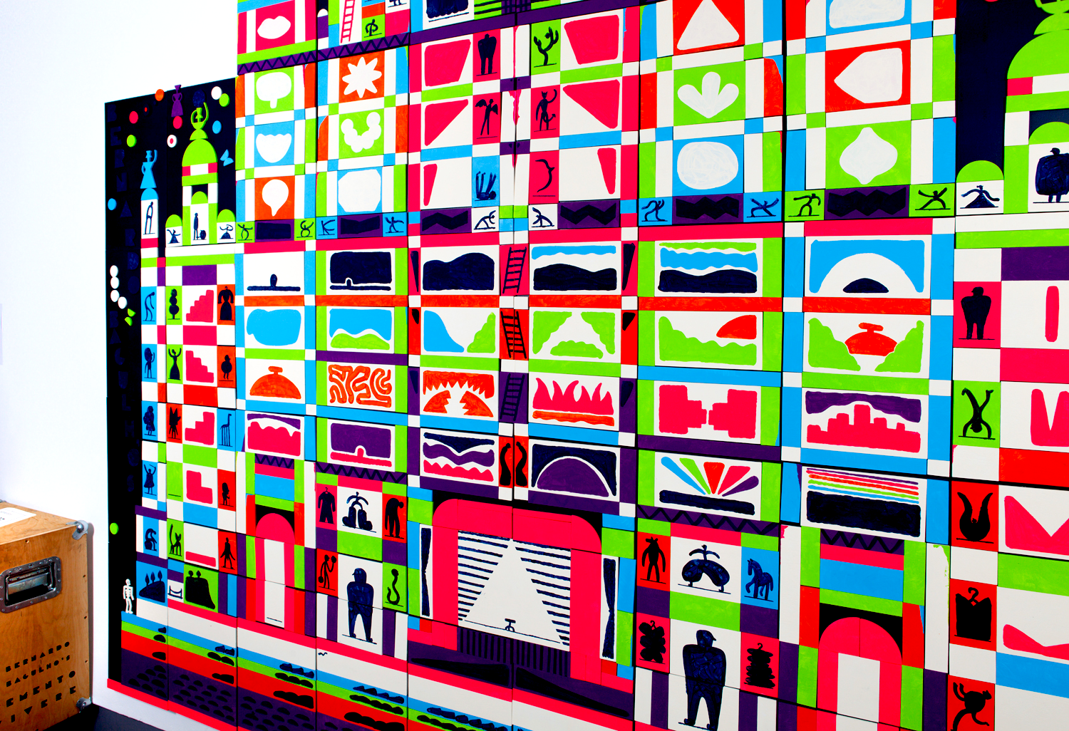 Colorful abstract art mural composed of many small tiles with various geometric shapes, silhouettes, and patterns in bright red, green, blue, purple, black, and white.
