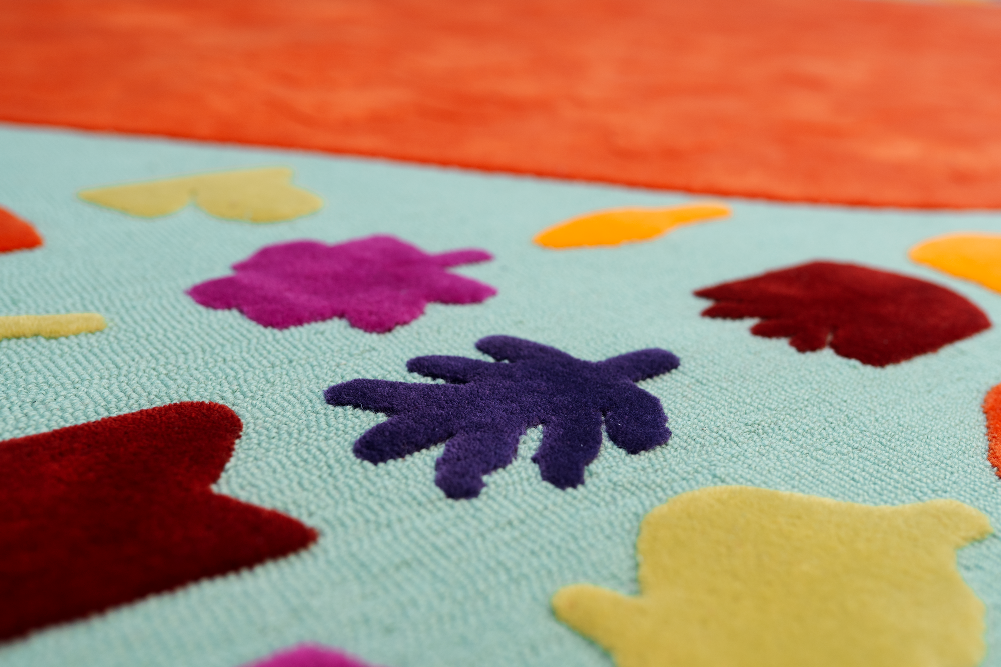 Close-up of a colorful, textured fabric with various foam shapes, including purple, yellow, orange, red, and pink, on a light blue background.