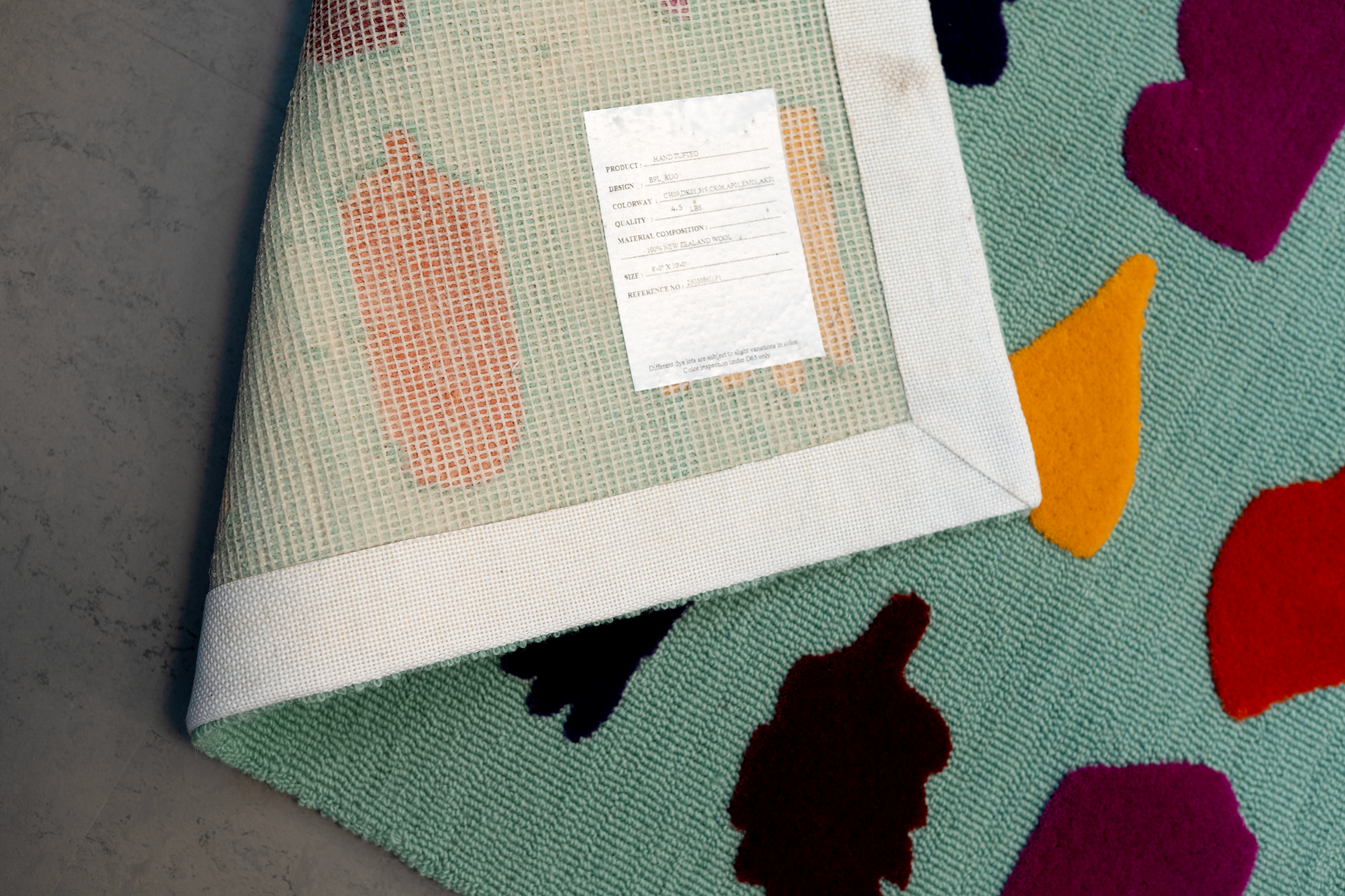 Close-up of a colorful rug with a tag on the corner, showing a pattern of various shapes and bright colors.
