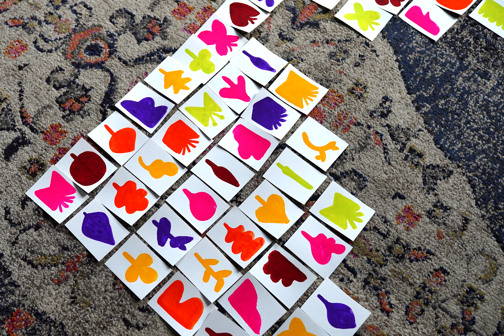 Colorful paper cutouts of various shapes like hearts, butterflies, and abstract designs are scattered on a textured, patterned carpet.
