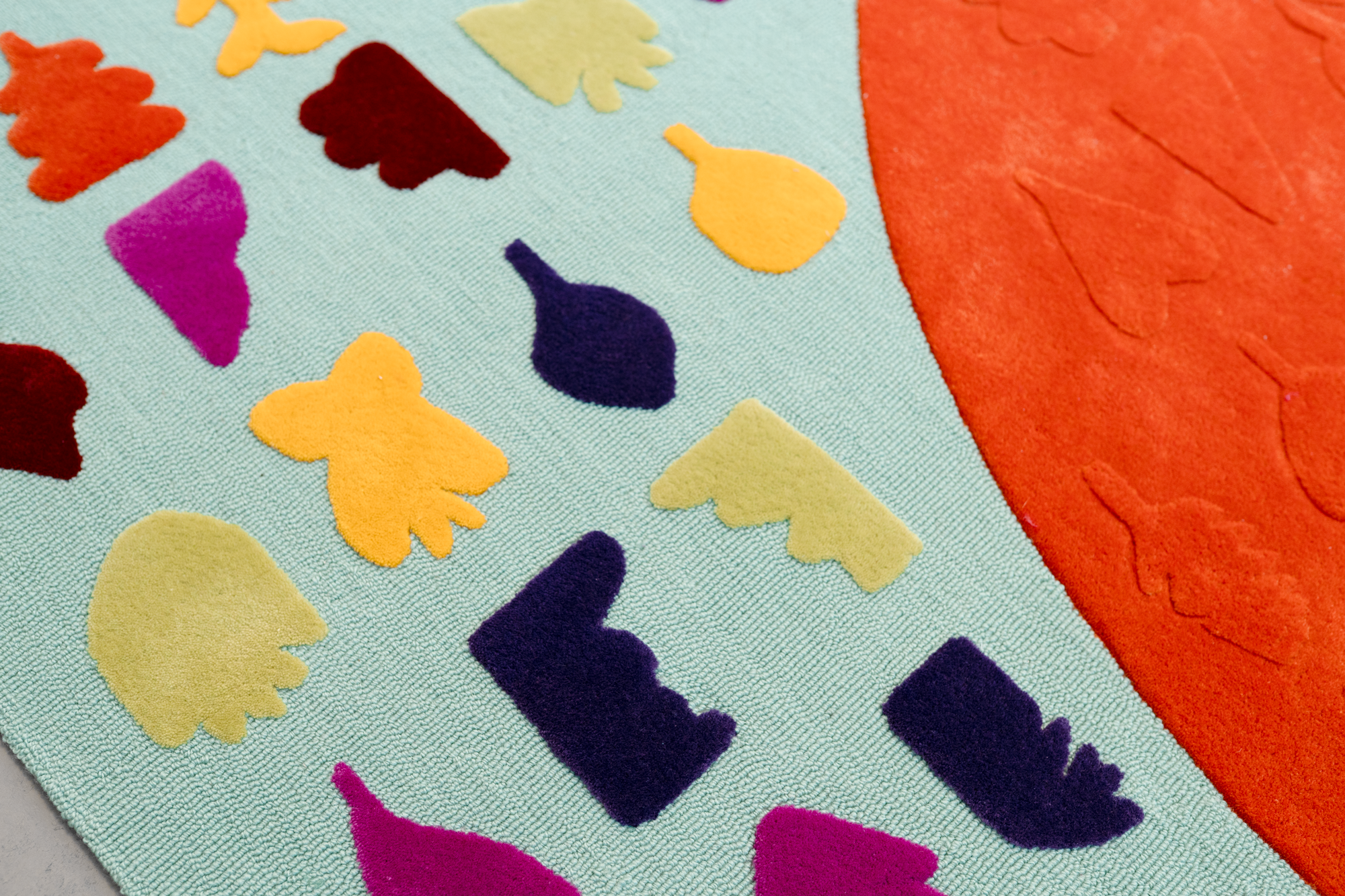Close-up of a colorful felt rug with cut-out butterfly and letter shapes on a blue background, with an orange border on the right side.