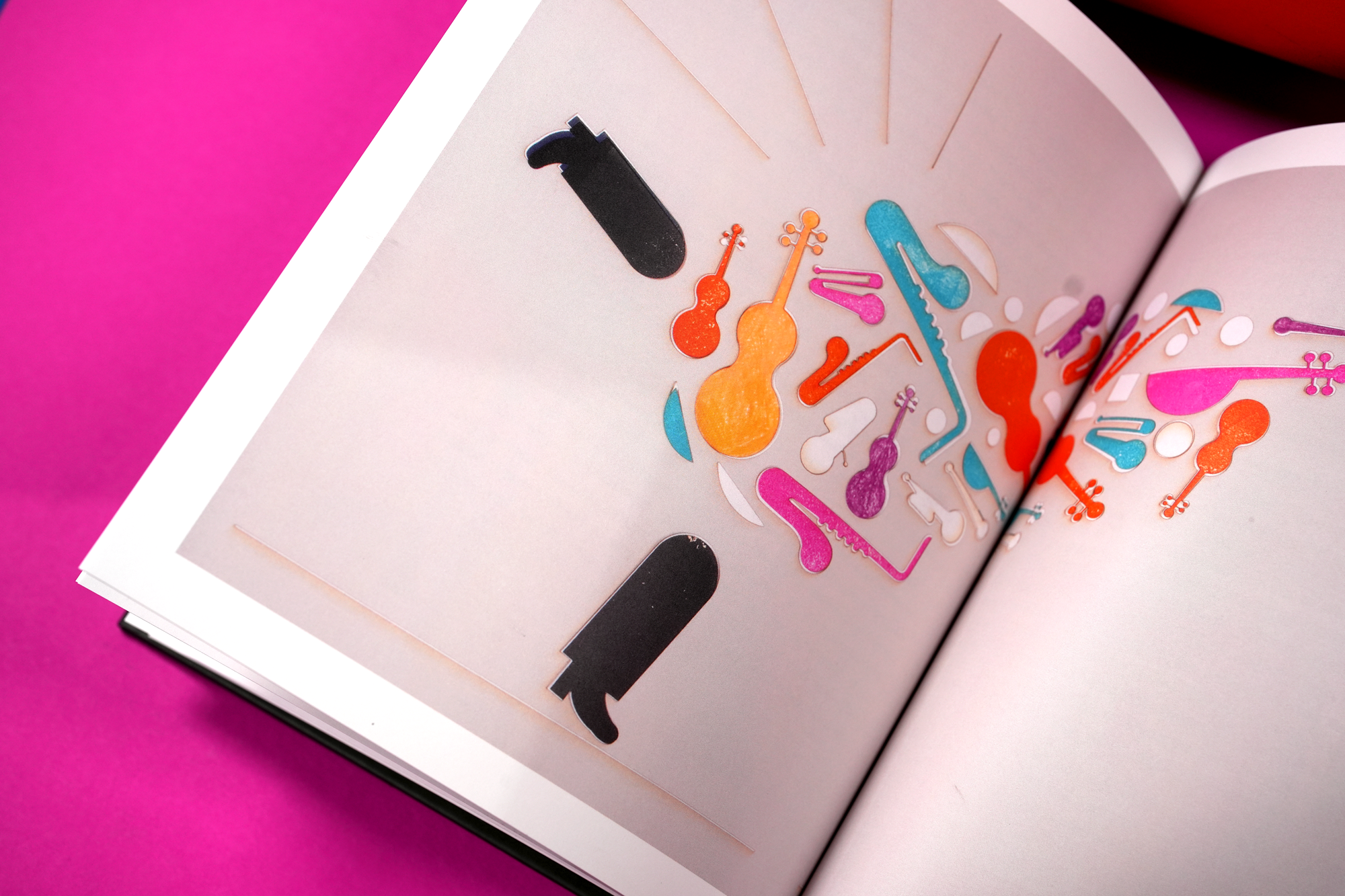 Open book with colorful guitar-shaped stickers on its pages, placed on a pink background.