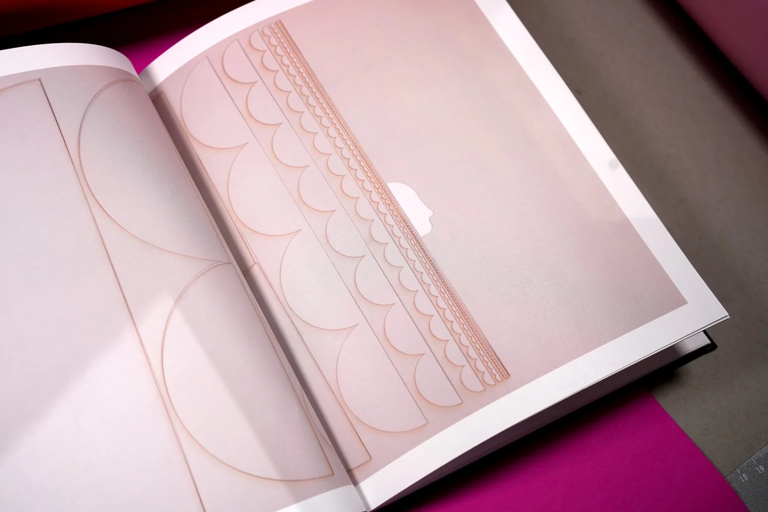Open book showing detailed, rose gold-colored, ornamental designs and patterns on a pink background.