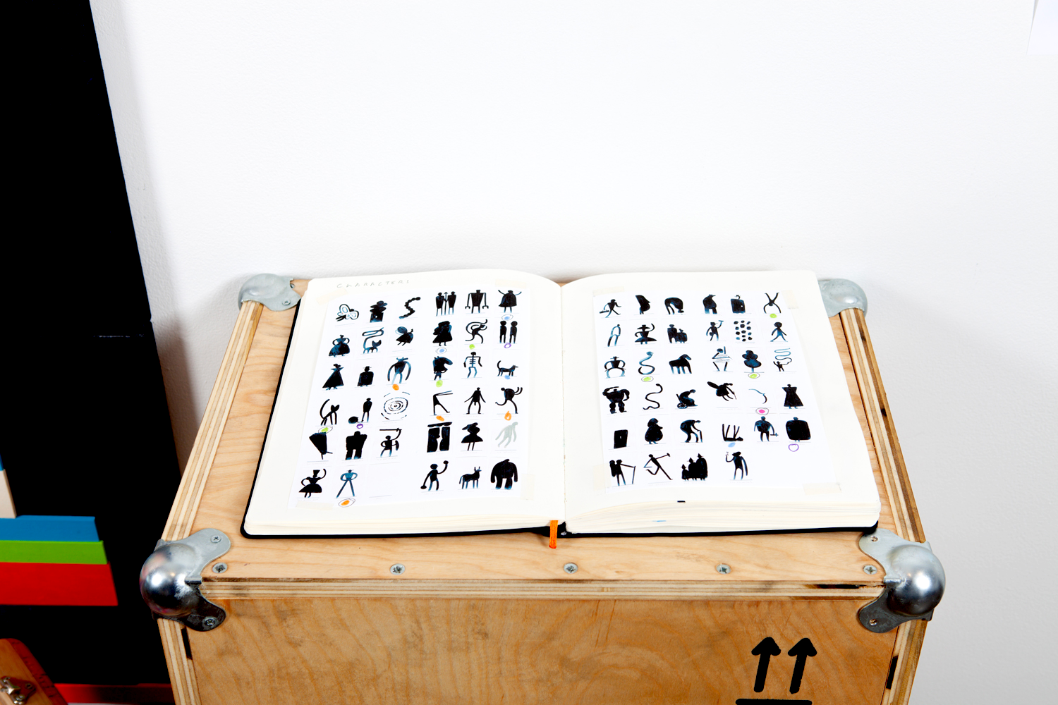 Open book displaying various black silhouette characters and objects on a wooden table.