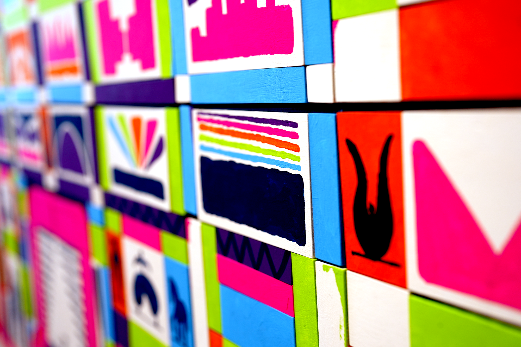 Close-up of colorful wooden alphabet blocks arranged in a grid, featuring various letters and vibrant colors such as pink, blue, green, orange, and black.