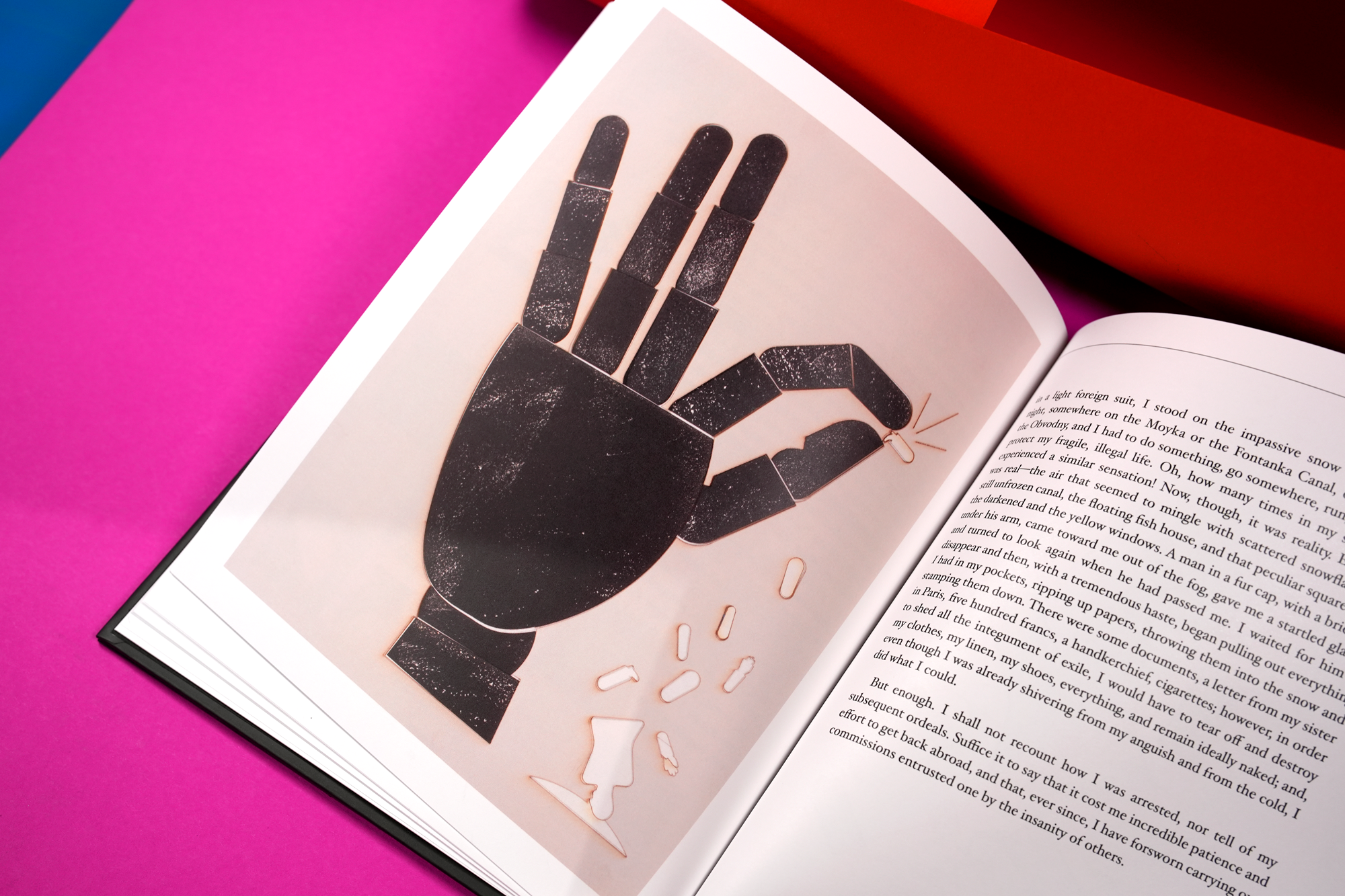 An open magazine showing an illustration of a black robotic hand making the peace sign, with some scattered paper clips around it, placed on a bright pink surface.