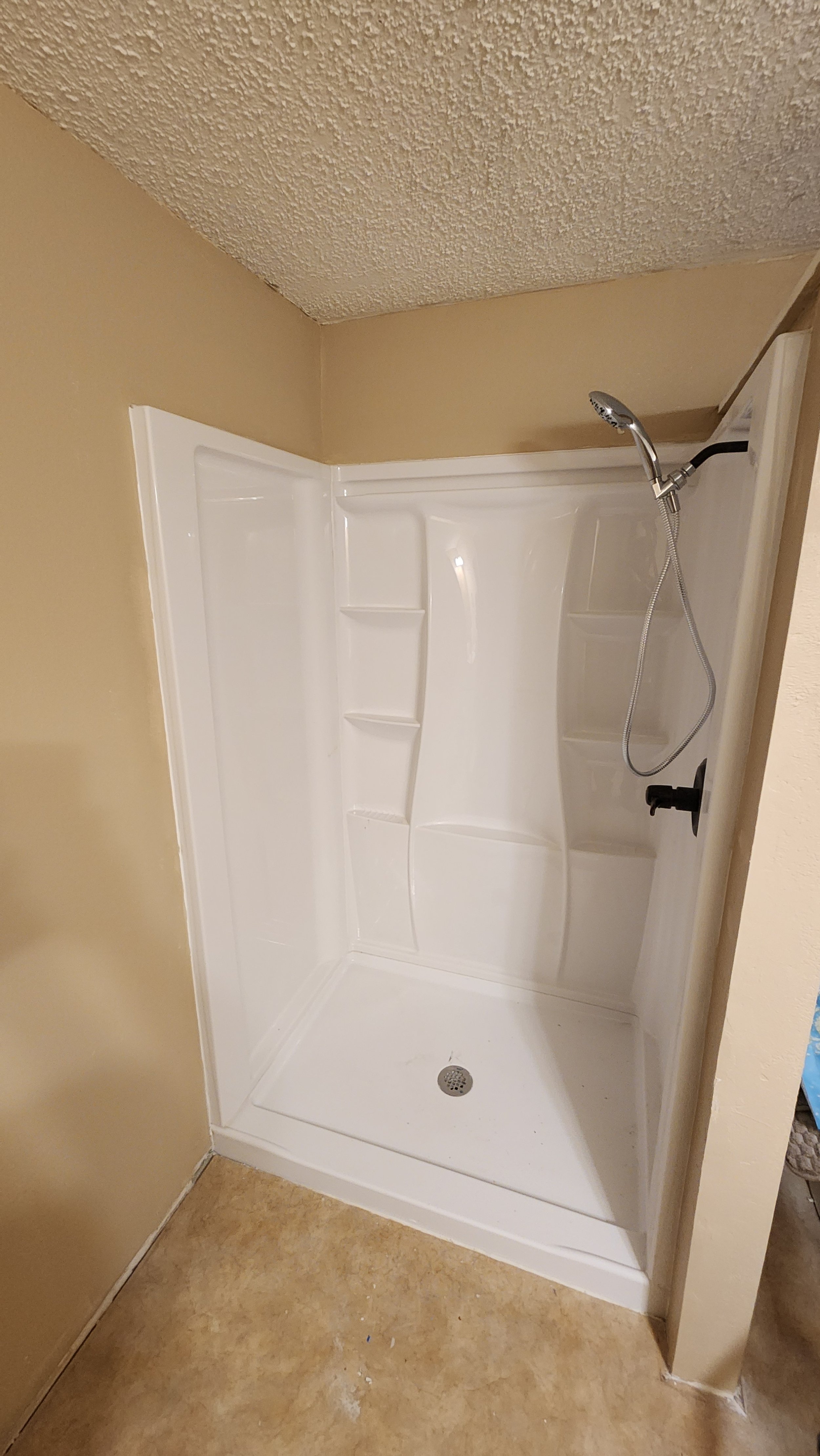 Empty white shower stall with built-in shelves, a handheld shower head, and a drain on the floor.