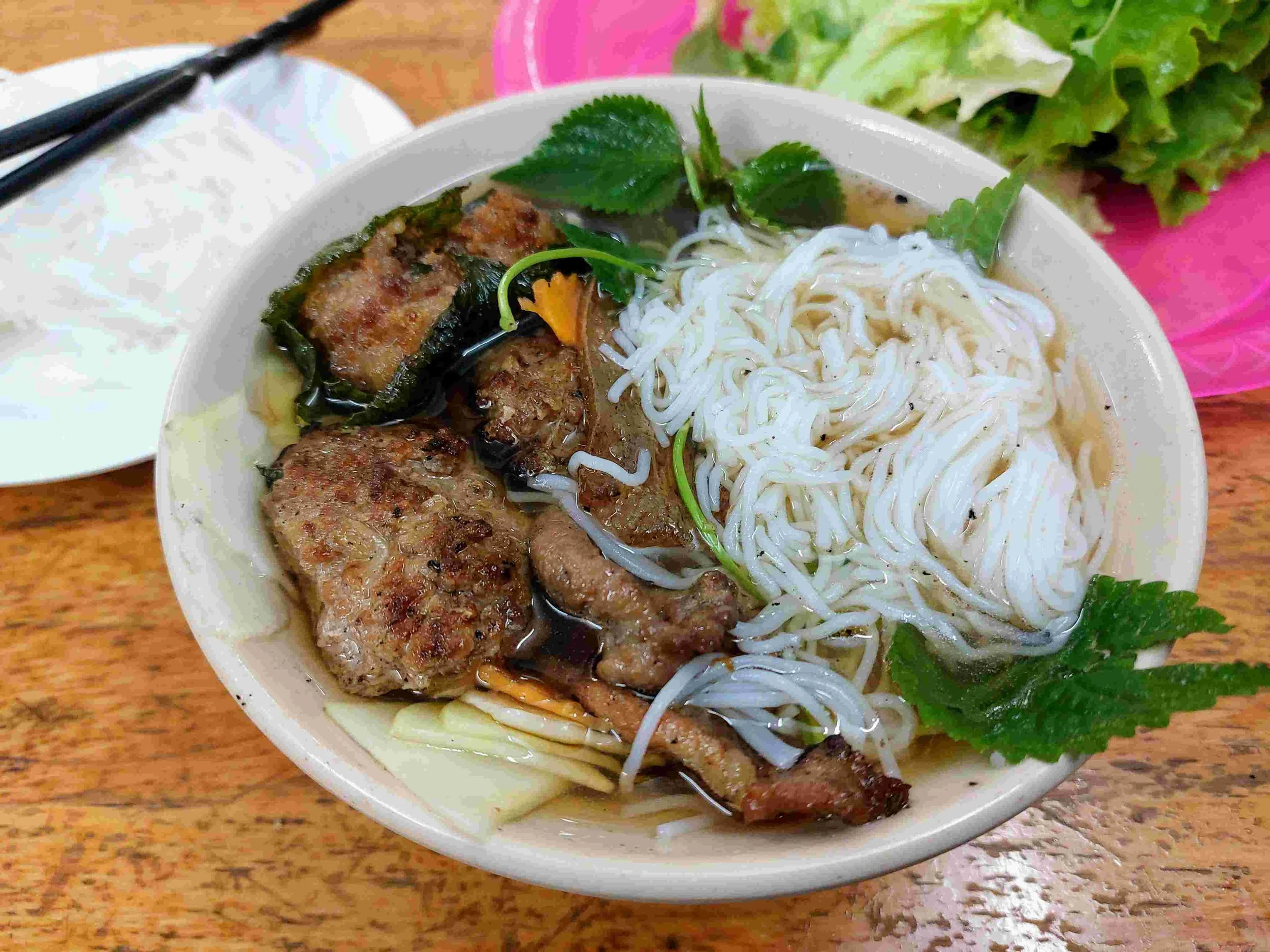 Grilled pork patties and sliced pork belly served with bún (vermicelli noodles), herbs, and nước chấm