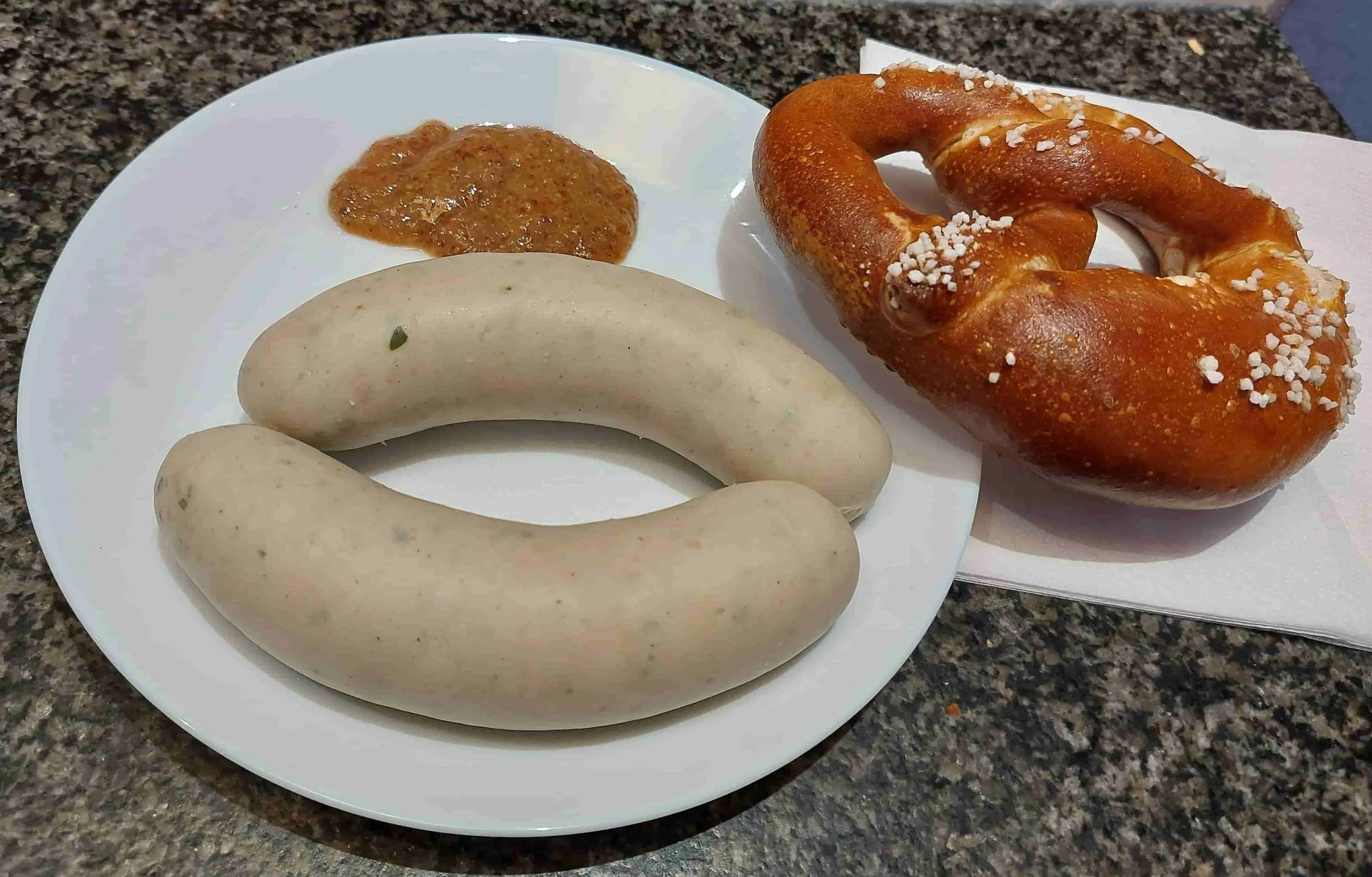 Two traditional Bavarian Weißwurst veal and pork sausages served with sweet mustard and pretzel