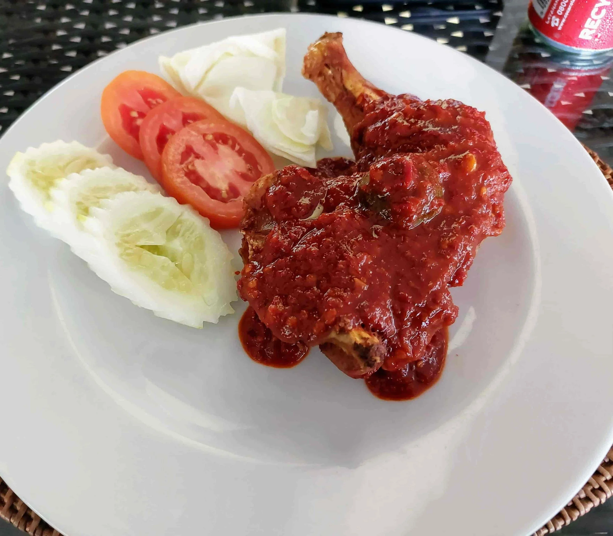 Traditional Ayam Plecing grilled chicken with tangy chili sauce, accompanied by sliced tomatoes and cucumbers